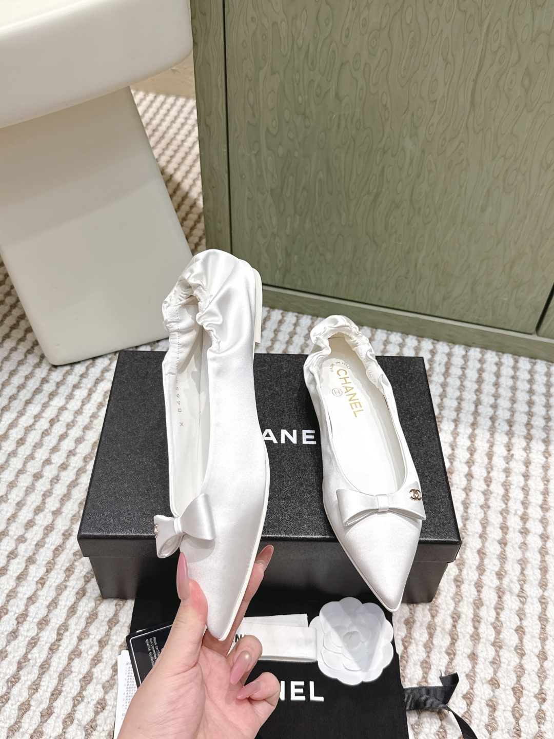 Pair of elegant Chanel white satin pointed-toe ballerina flats with bows and gold logos on a black box. - Hình 4