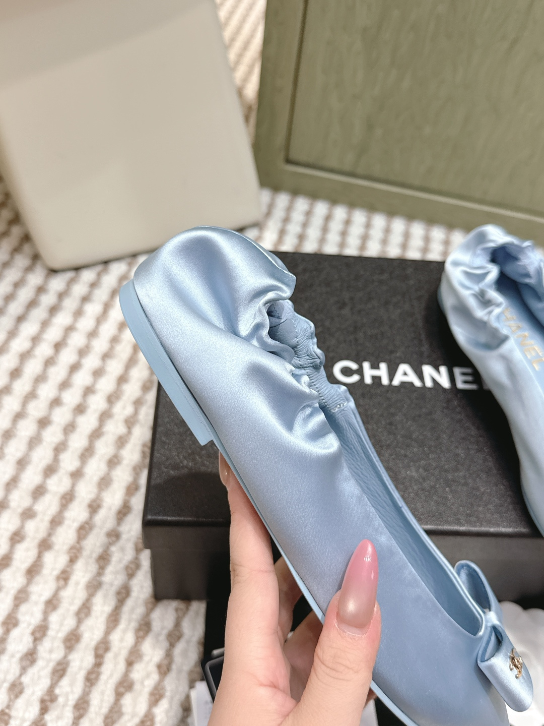 A pair of light blue Chanel satin pointed-toe ballet flats with a bow and gold logo detail, sitting on a black Chanel shoe box. - Hình 8