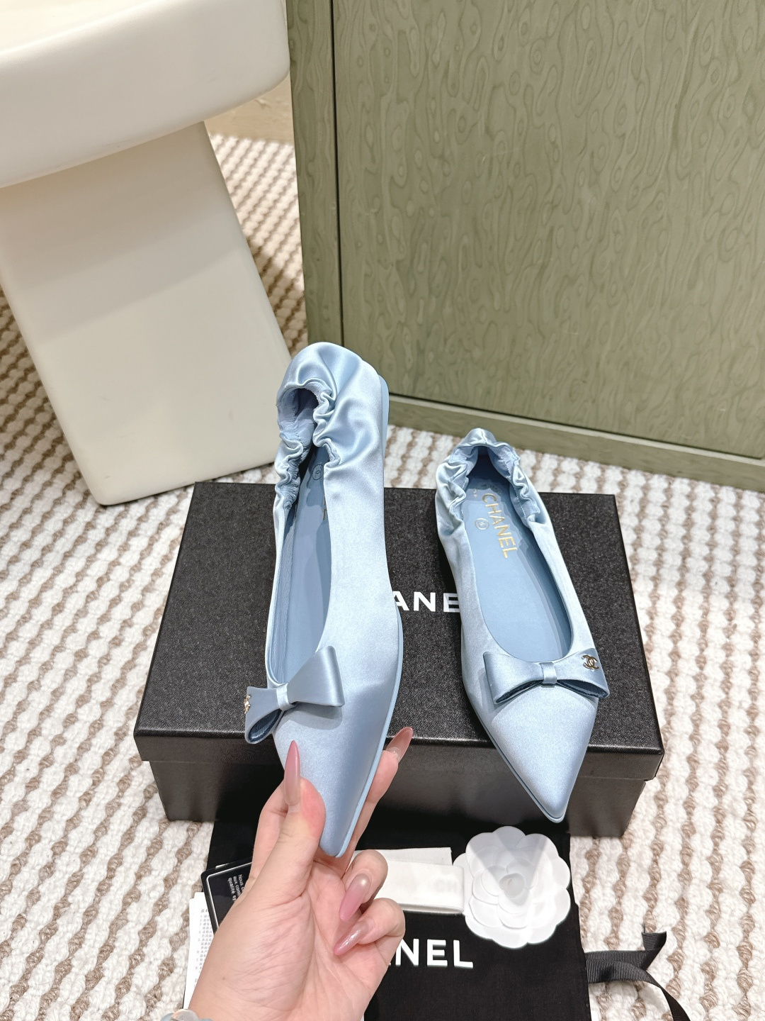 A pair of light blue Chanel satin pointed-toe ballet flats with a bow and gold logo detail, sitting on a black Chanel shoe box. - Hình 4