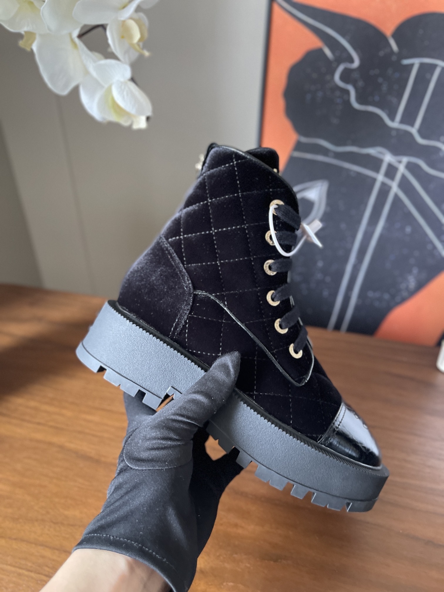 A pair of black Chanel quilted velvet combat boots with patent leather toe caps and gold lettering on a wooden surface. - Hình 7