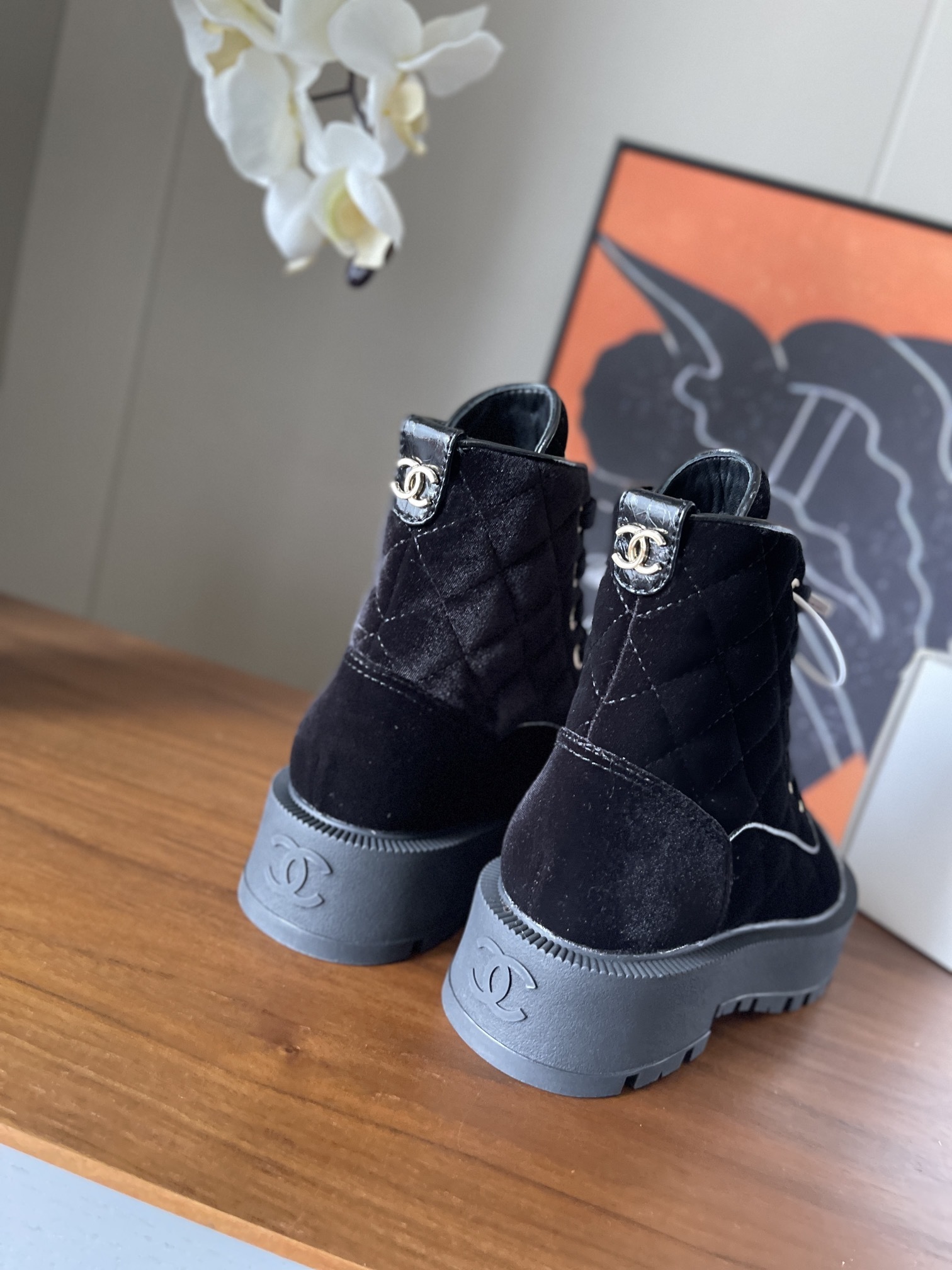 A pair of black Chanel quilted velvet combat boots with patent leather toe caps and gold lettering on a wooden surface. - Hình 5
