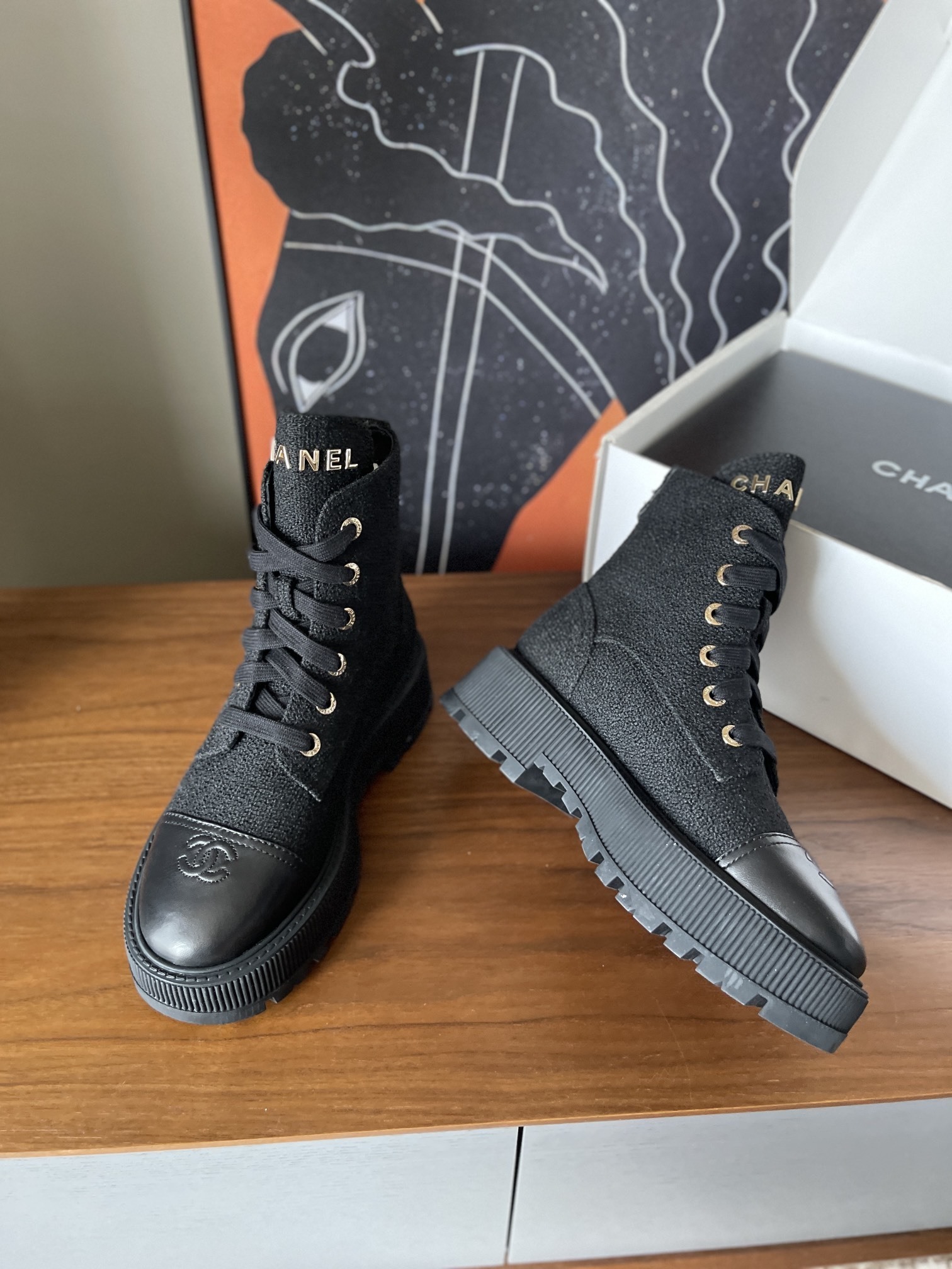 A pair of Chanel black tweed lace-up combat boots with gold lettering and chunky platform soles placed on a wooden surface. - Hình 9