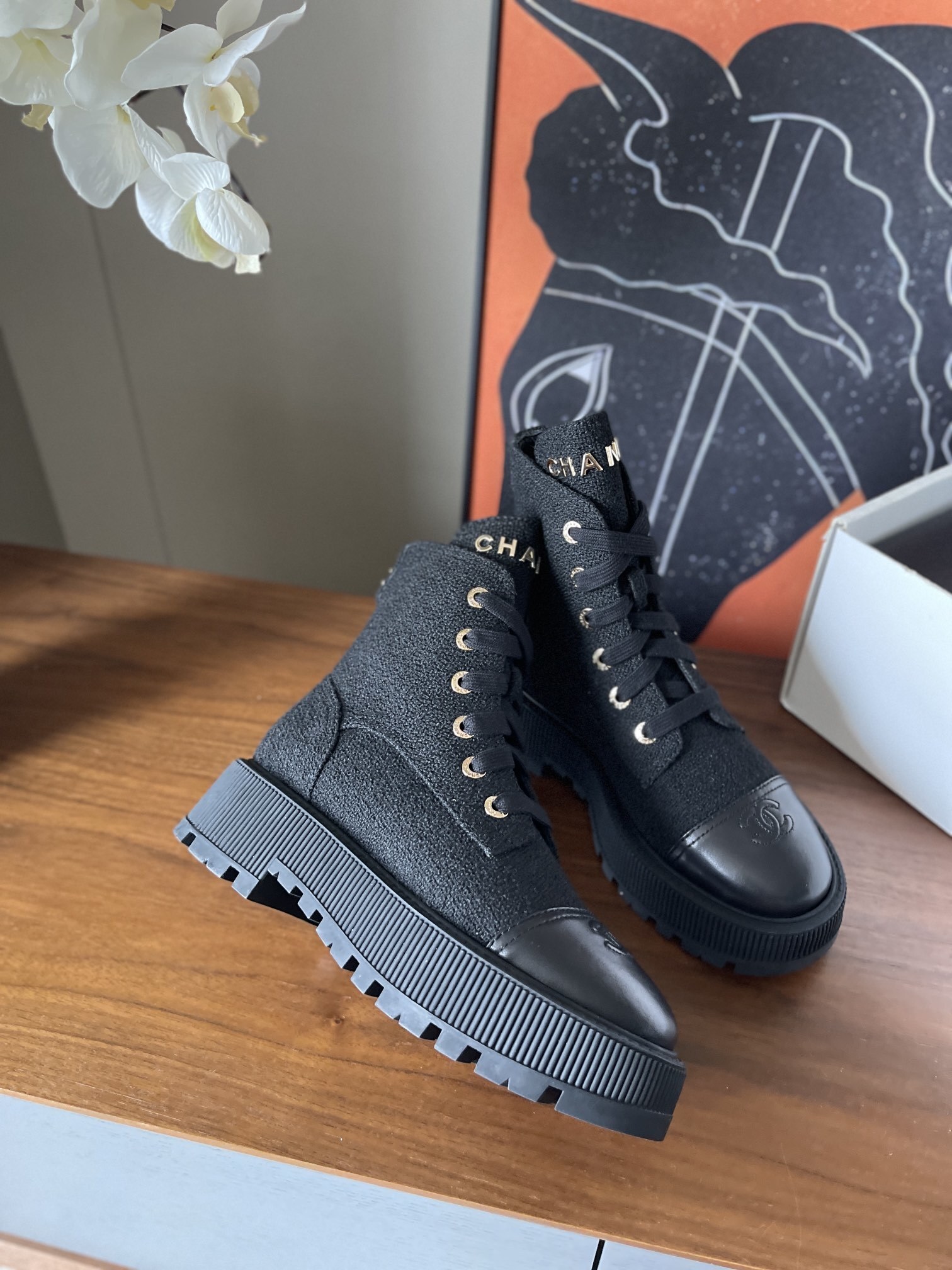 A pair of Chanel black tweed lace-up combat boots with gold lettering and chunky platform soles placed on a wooden surface. - Hình 3