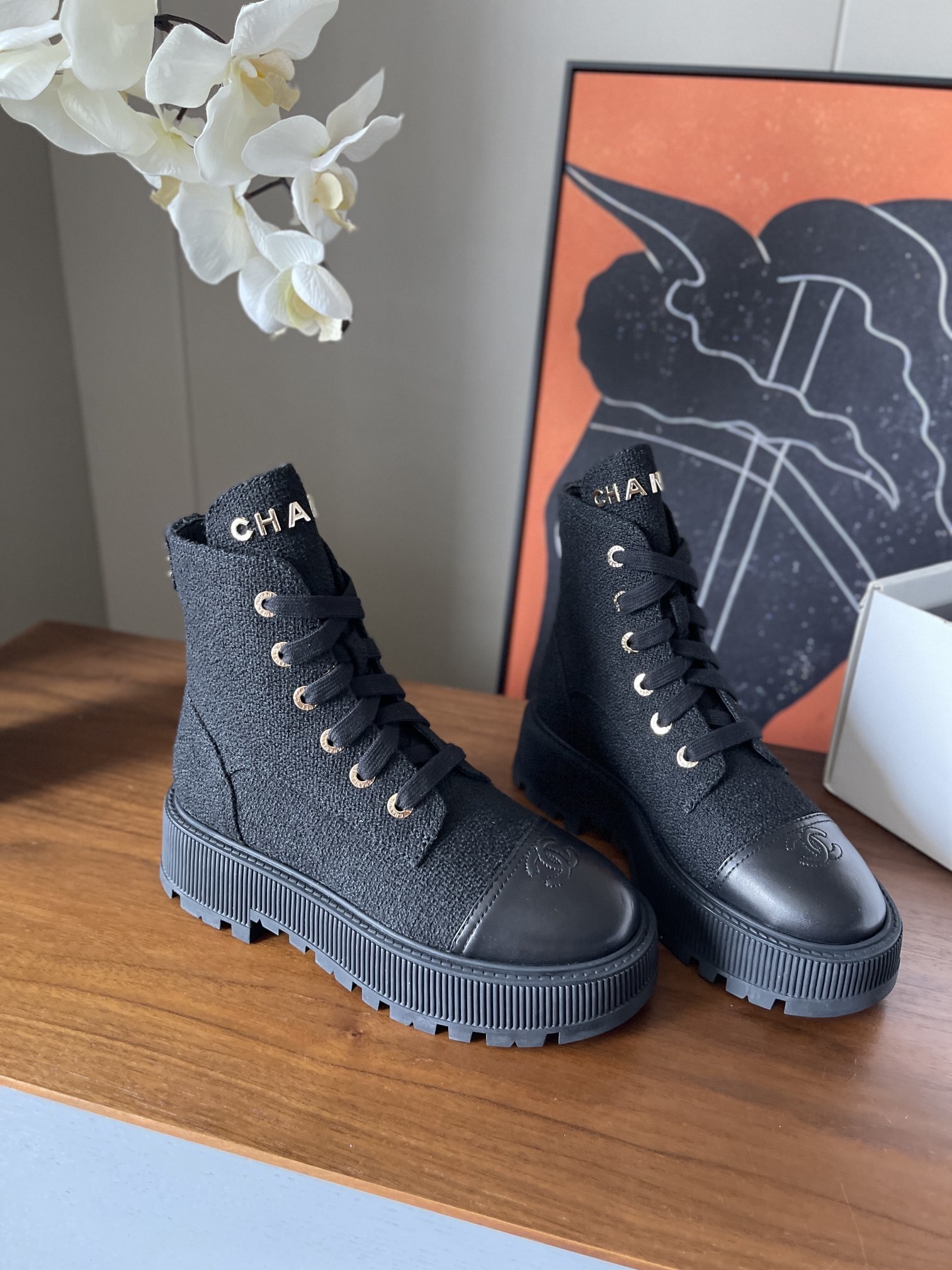 A pair of Chanel black tweed lace-up combat boots with gold lettering and chunky platform soles placed on a wooden surface. - Hình 2
