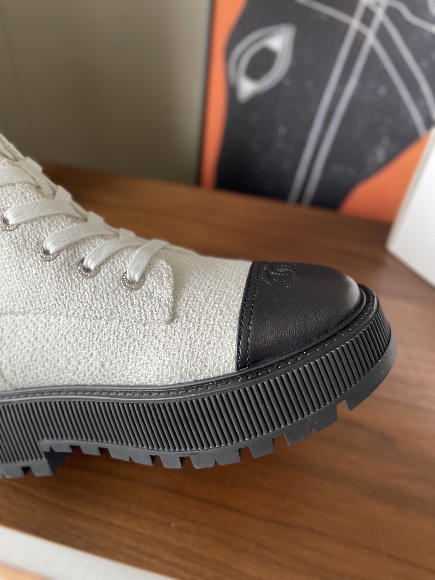 Pair of Chanel white tweed ankle boots with black leather toe caps and chunky black platform soles on a wooden surface. - Hình 6