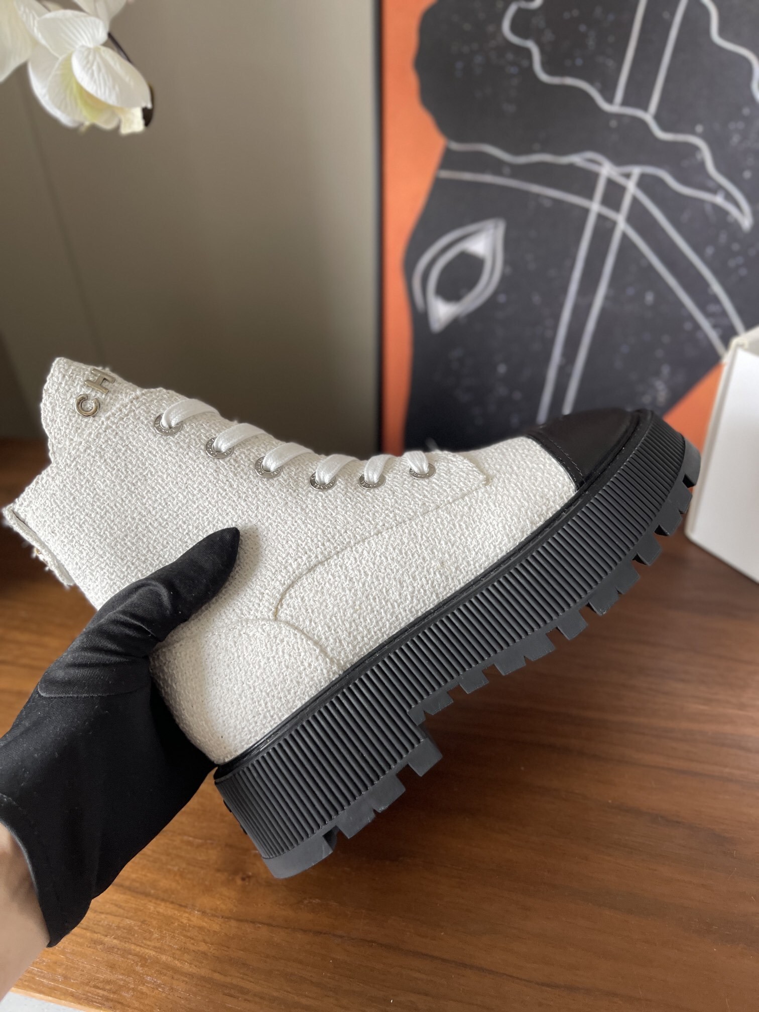 Pair of Chanel white tweed ankle boots with black leather toe caps and chunky black platform soles on a wooden surface. - Hình 5