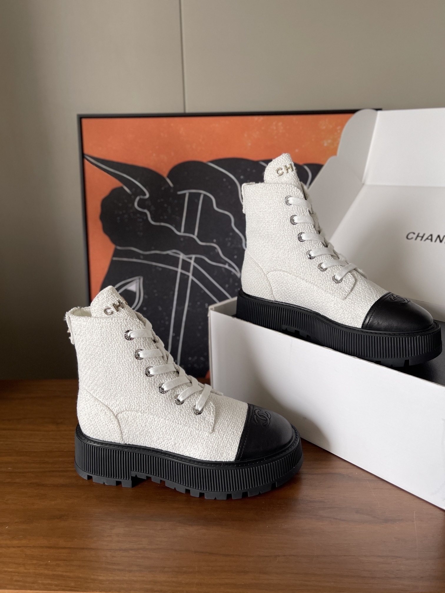 Pair of Chanel white tweed ankle boots with black leather toe caps and chunky black platform soles on a wooden surface. - Hình 4