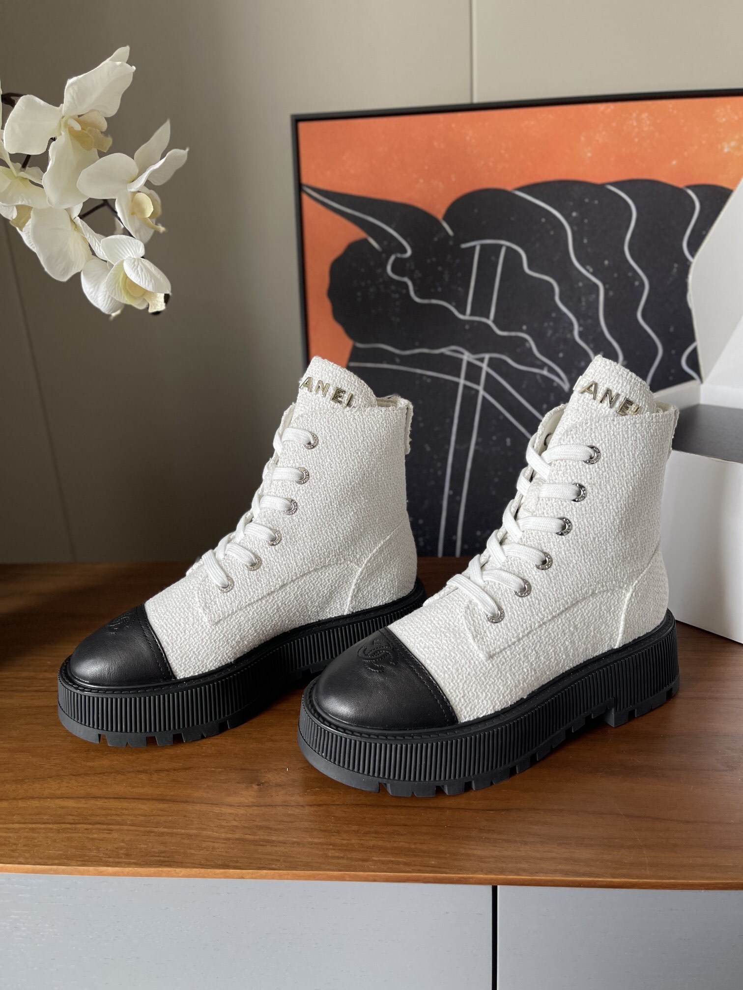 Pair of Chanel white tweed ankle boots with black leather toe caps and chunky black platform soles on a wooden surface. - Hình 3