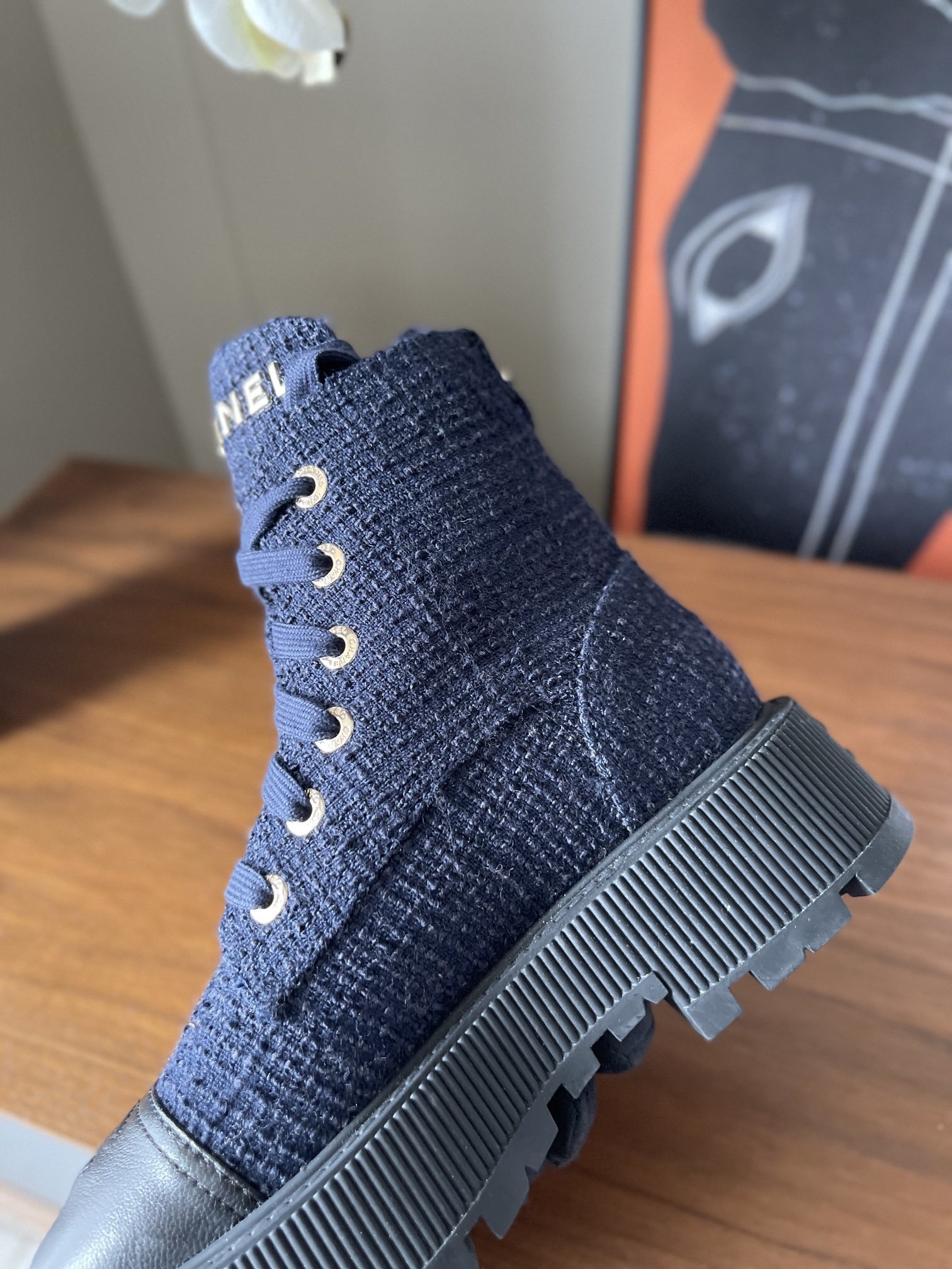 Pair of Chanel navy blue tweed lace-up ankle boots with black leather toe caps and gold lettering on a wooden surface. - Hình 7