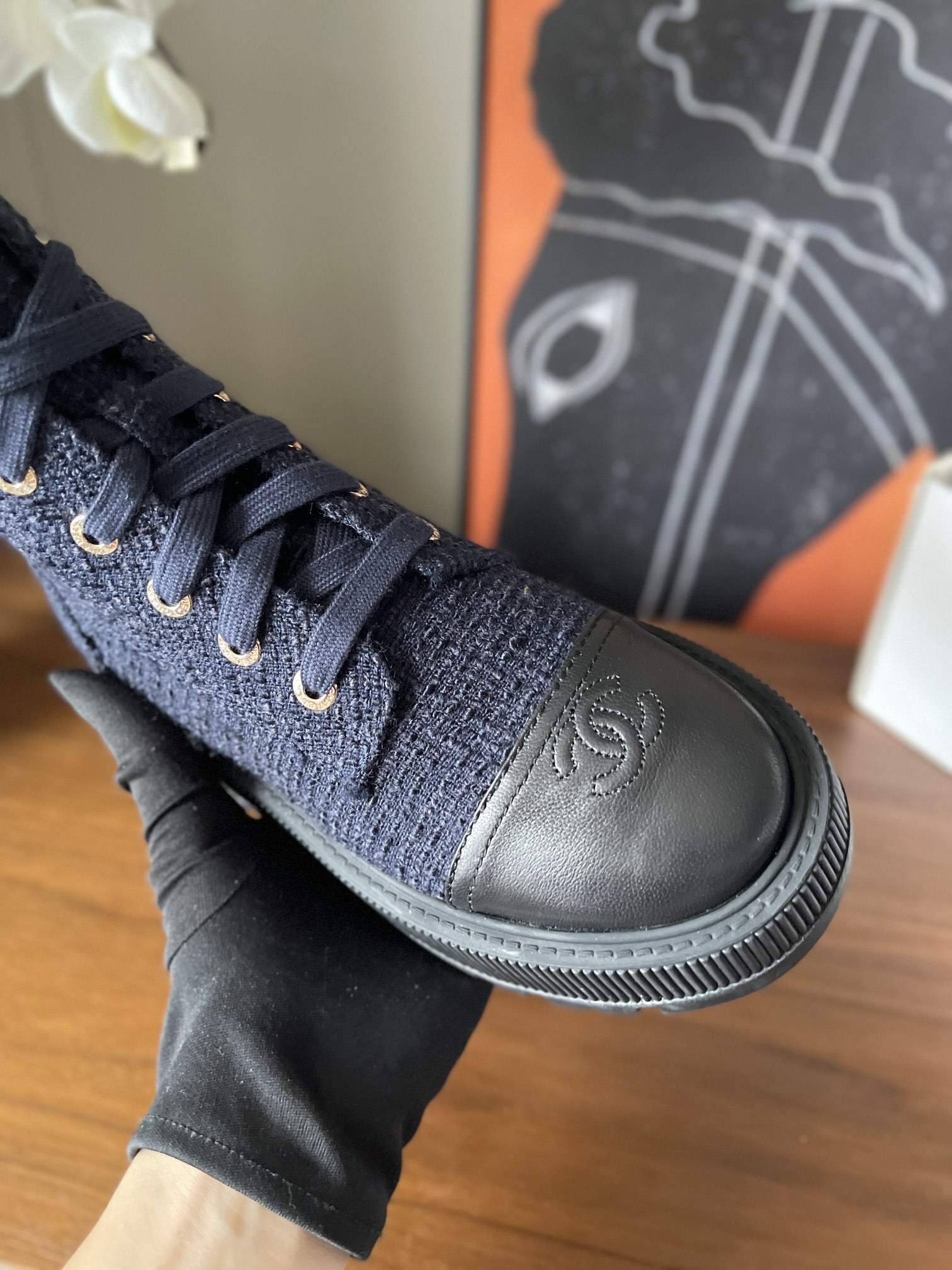 Pair of Chanel navy blue tweed lace-up ankle boots with black leather toe caps and gold lettering on a wooden surface. - Hình 6