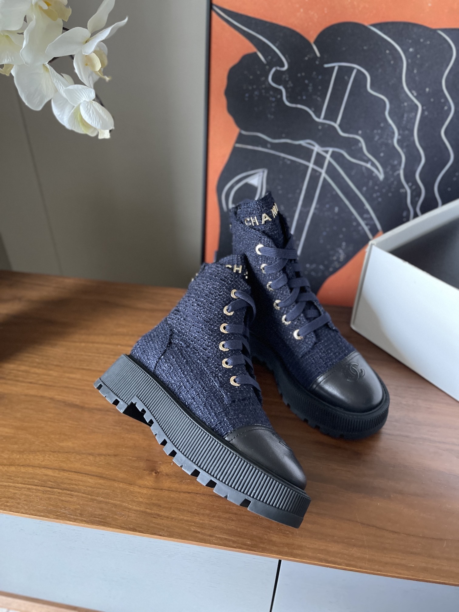 Pair of Chanel navy blue tweed lace-up ankle boots with black leather toe caps and gold lettering on a wooden surface. - Hình 4