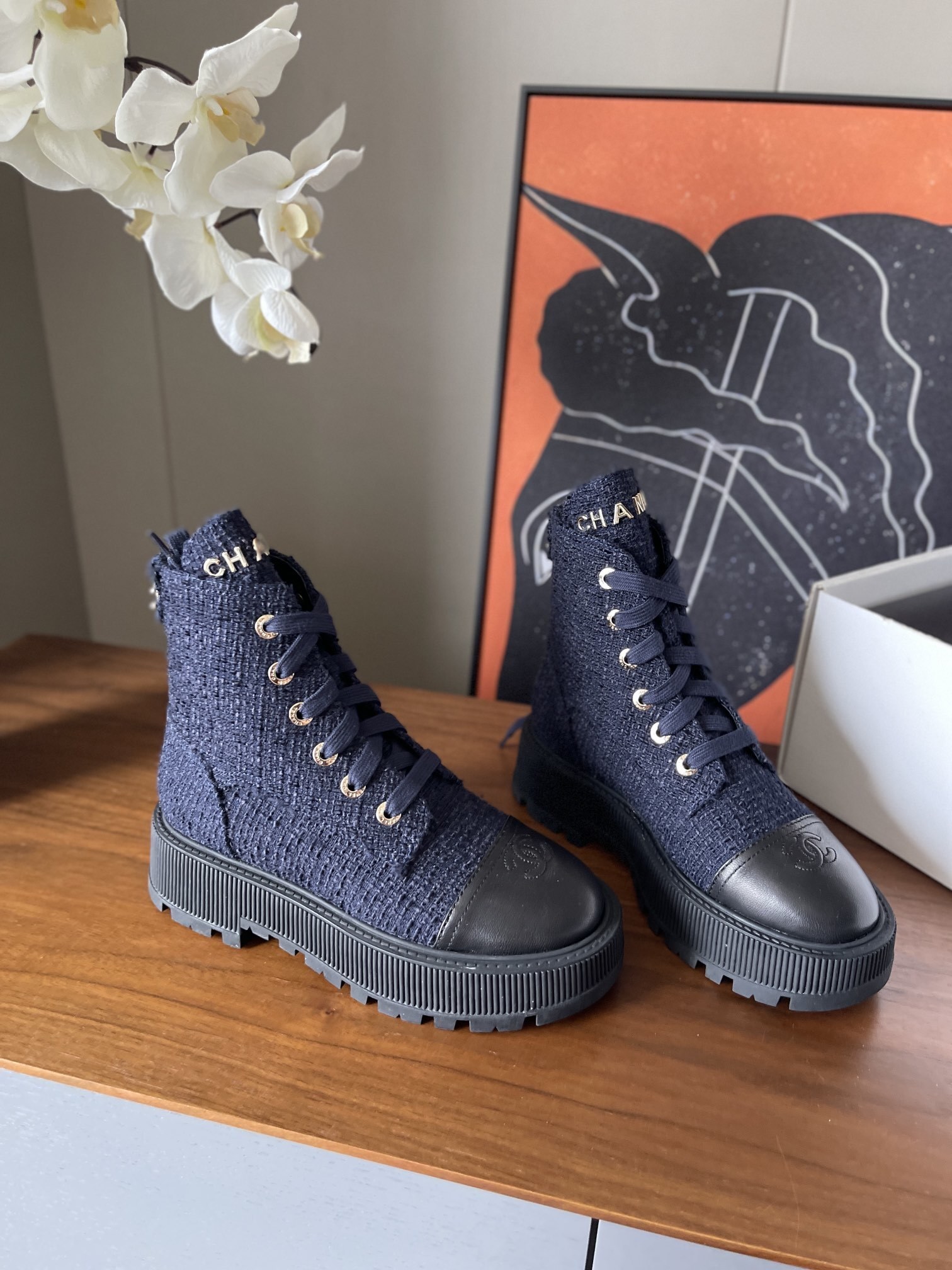 Pair of Chanel navy blue tweed lace-up ankle boots with black leather toe caps and gold lettering on a wooden surface. - Hình 3