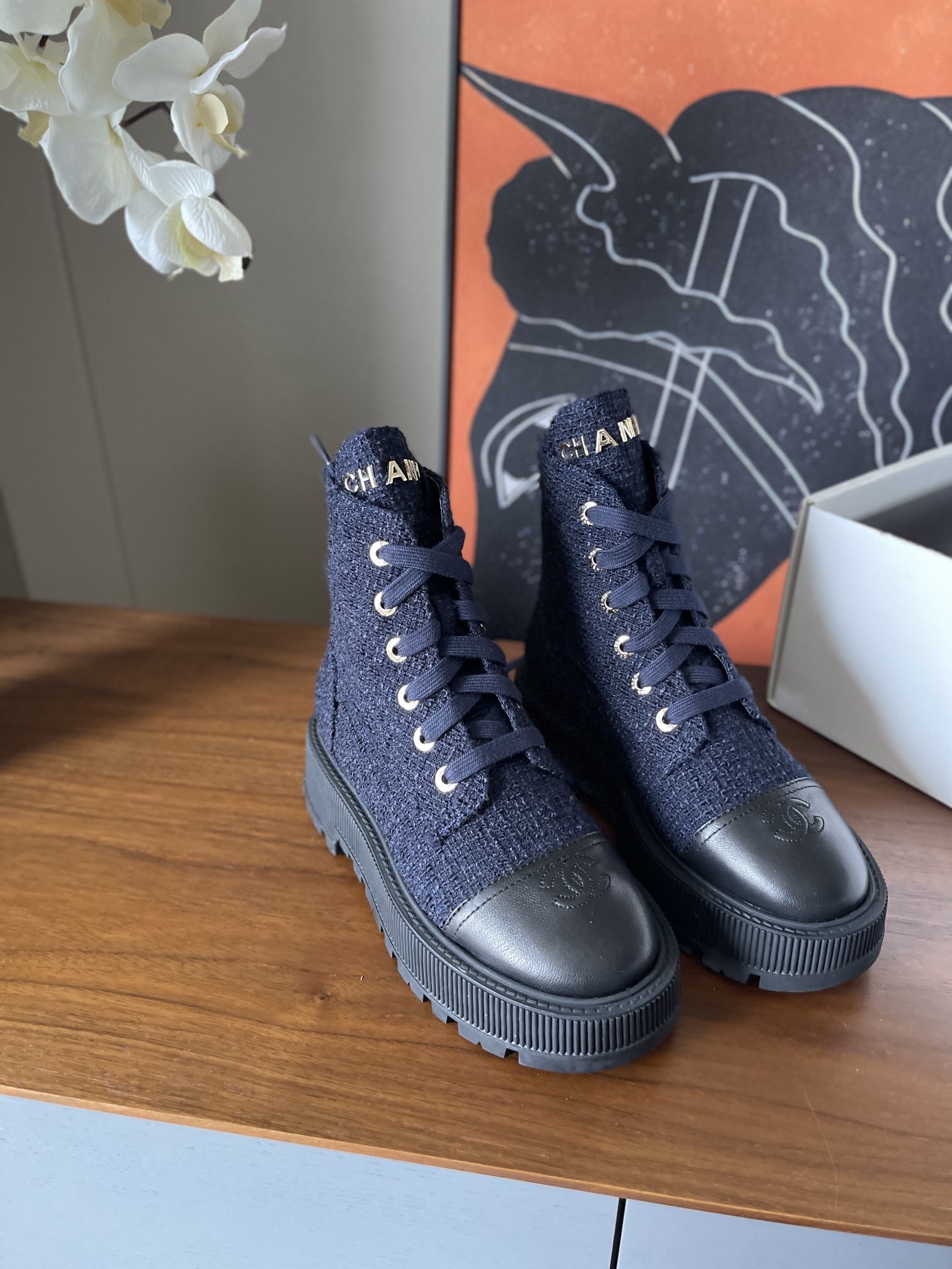 Pair of Chanel navy blue tweed lace-up ankle boots with black leather toe caps and gold lettering on a wooden surface. - Hình 2