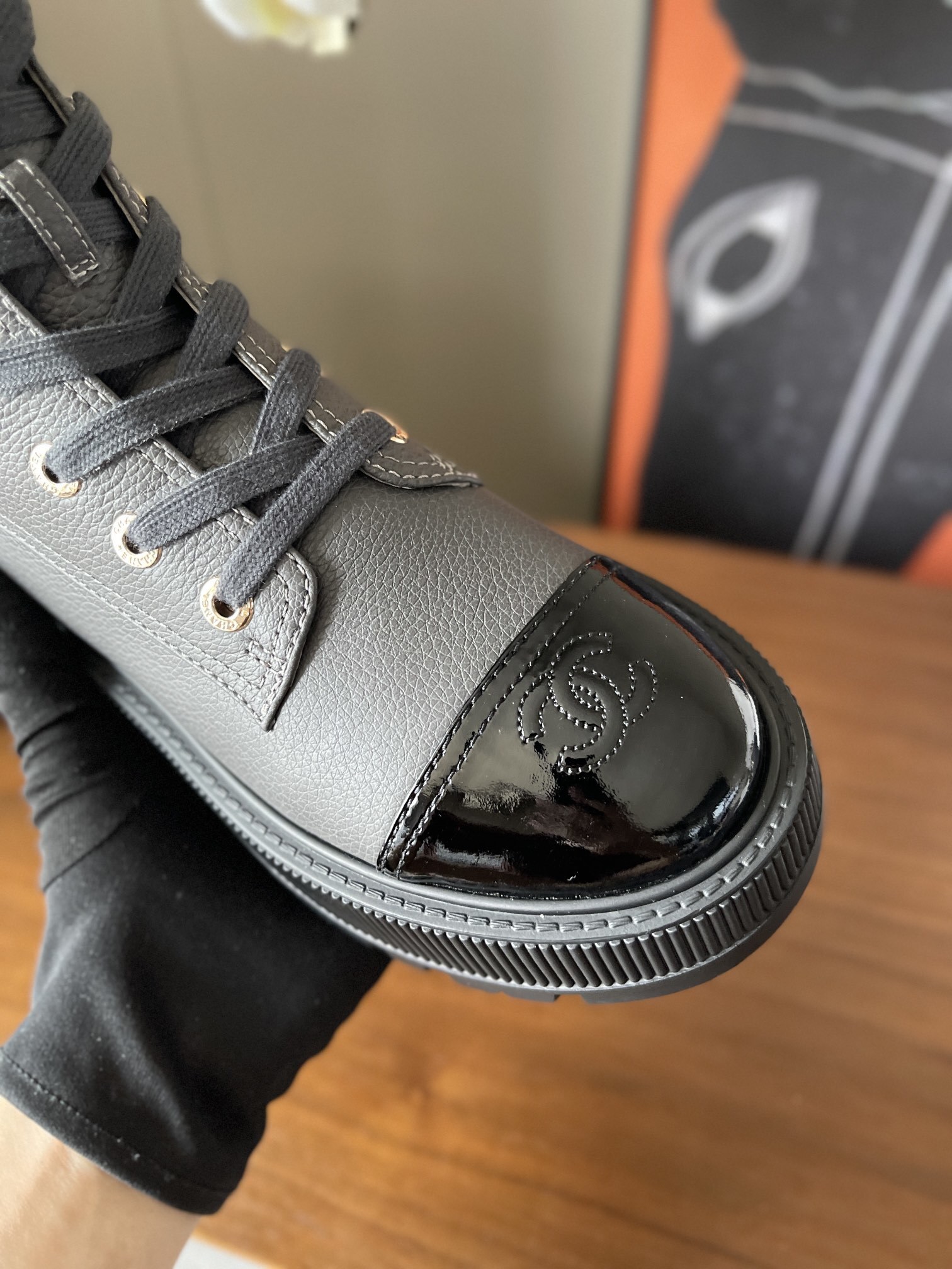 A pair of luxury grey pebbled leather ankle boots with black patent toe caps and thick black platform lug soles displayed on a wooden surface. - Hình 7