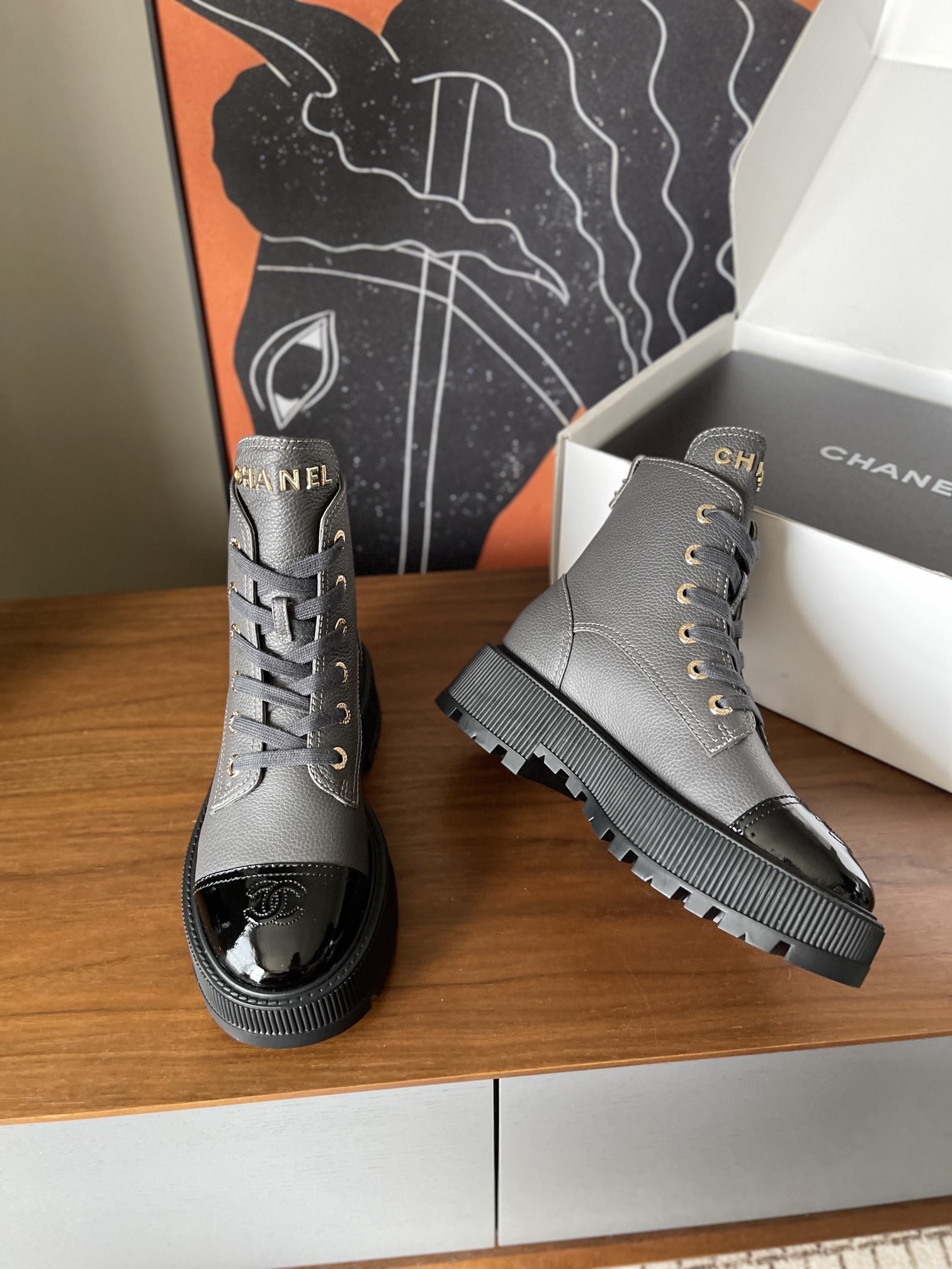 A pair of luxury grey pebbled leather ankle boots with black patent toe caps and thick black platform lug soles displayed on a wooden surface. - Hình 5