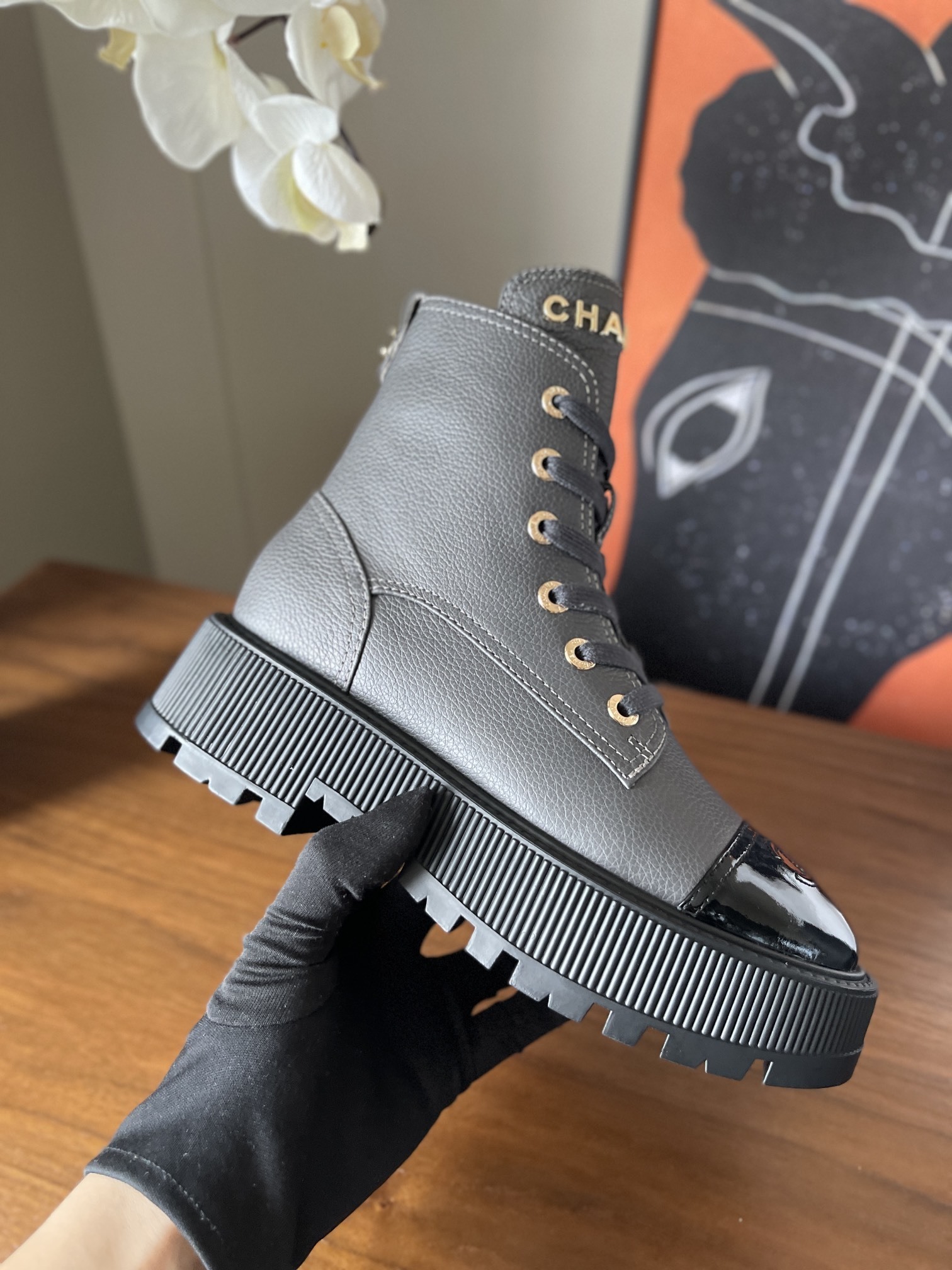 A pair of luxury grey pebbled leather ankle boots with black patent toe caps and thick black platform lug soles displayed on a wooden surface. - Hình 4