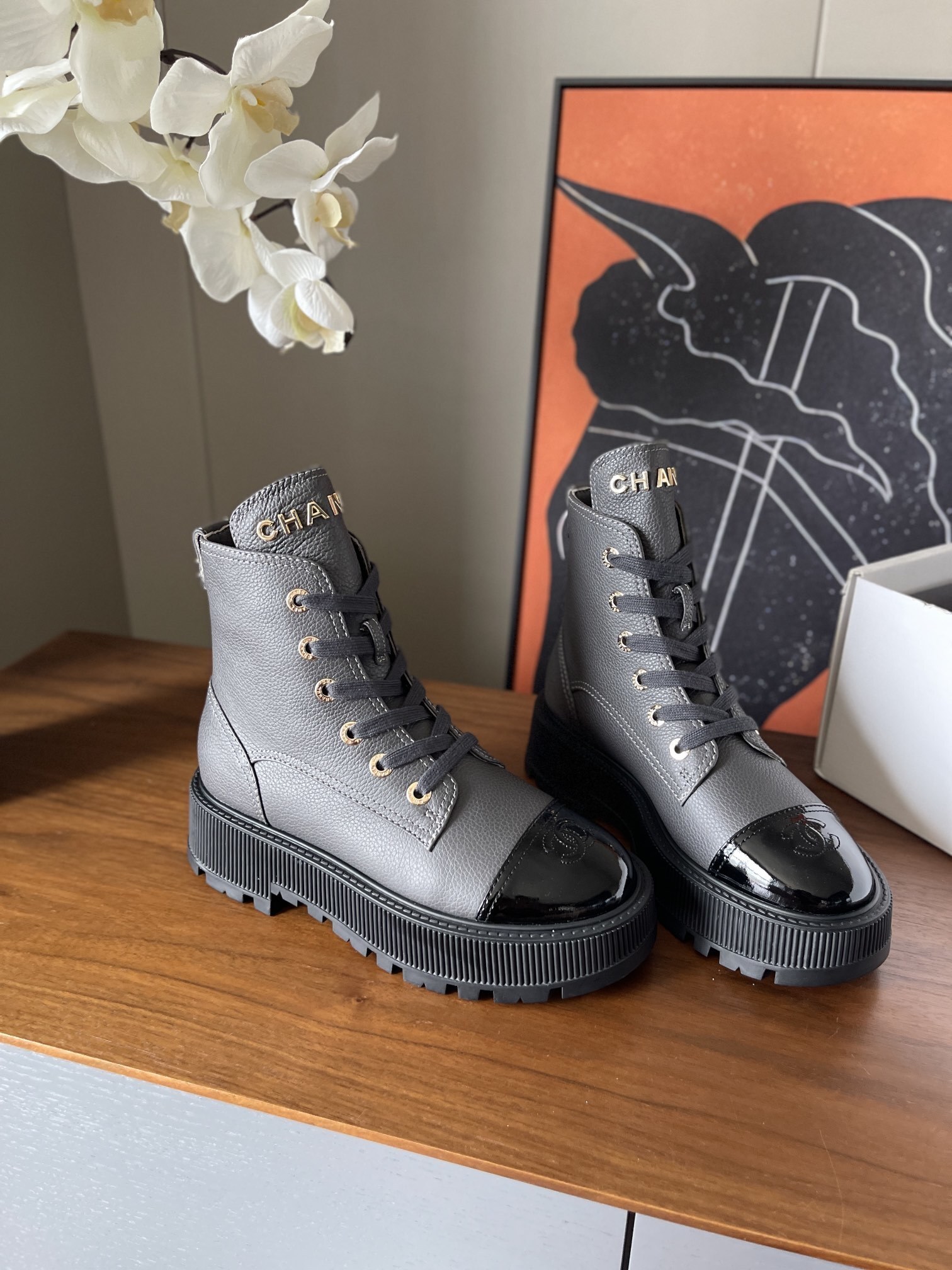 A pair of luxury grey pebbled leather ankle boots with black patent toe caps and thick black platform lug soles displayed on a wooden surface. - Hình 3