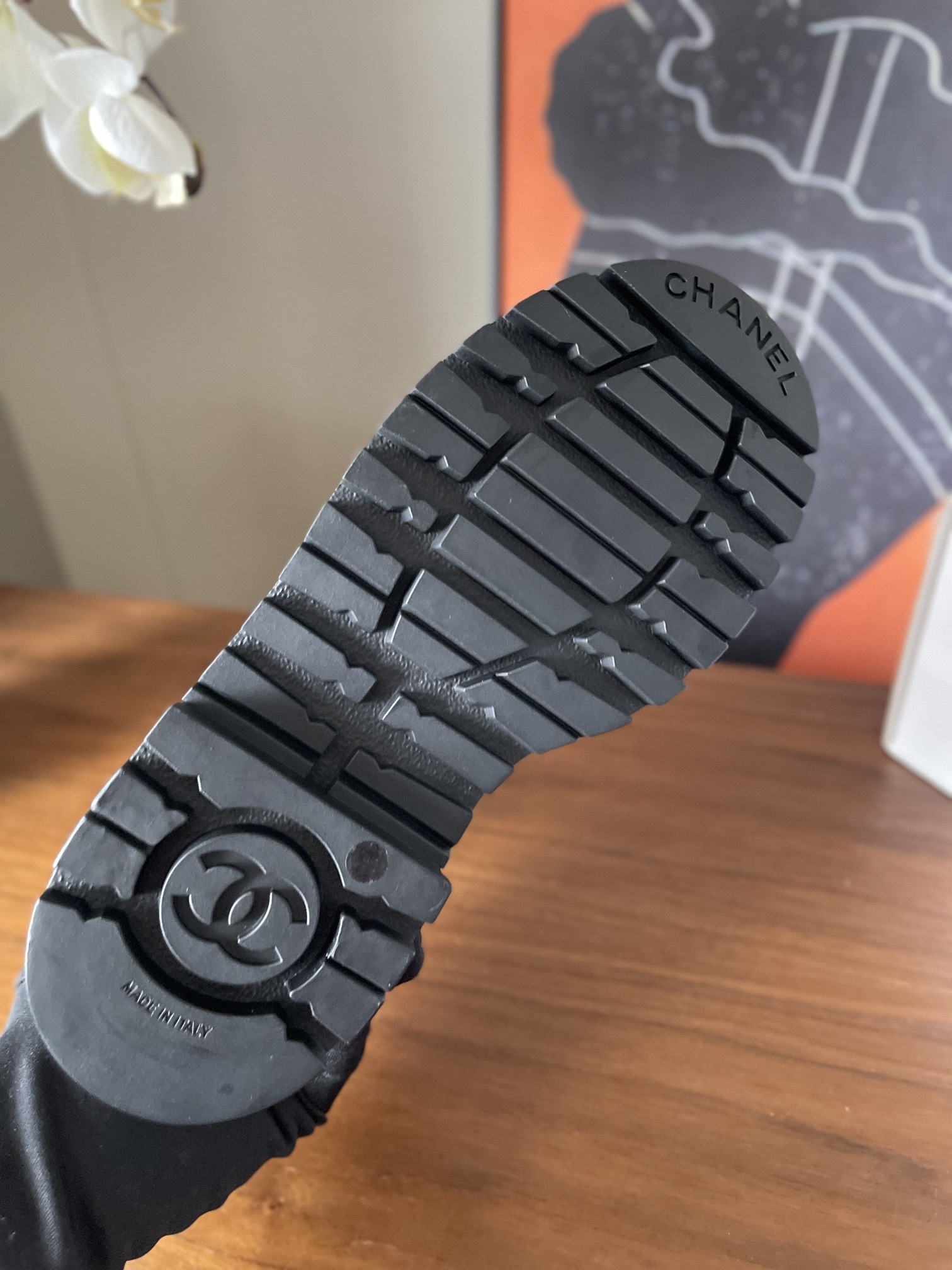 Pair of luxury white leather Chanel ankle boots with black toe caps and chunky platform soles on a wooden table. - Hình 9