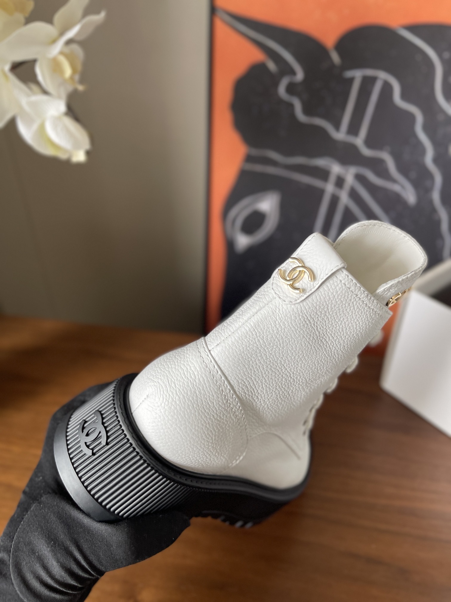 Pair of luxury white leather Chanel ankle boots with black toe caps and chunky platform soles on a wooden table. - Hình 8