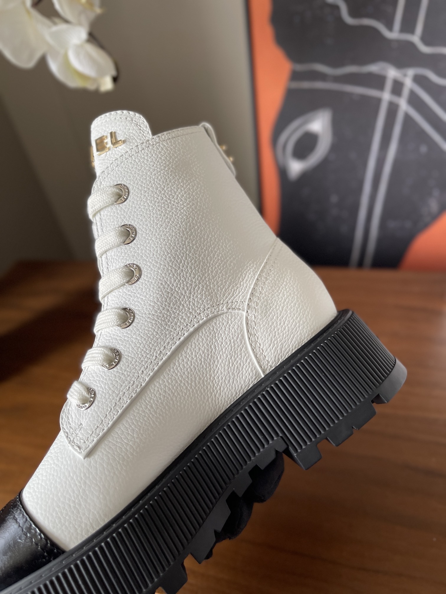 Pair of luxury white leather Chanel ankle boots with black toe caps and chunky platform soles on a wooden table. - Hình 7