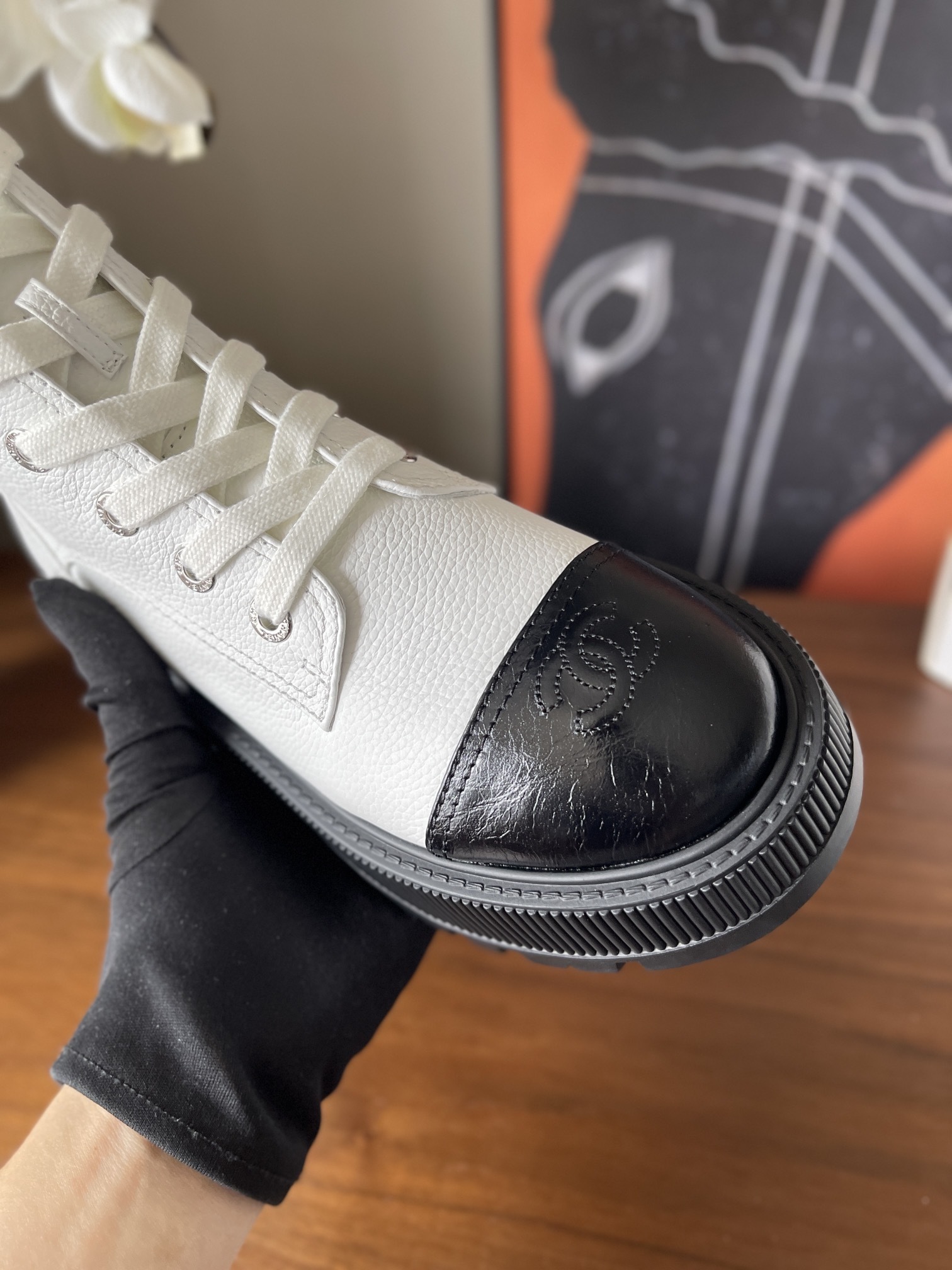 Pair of luxury white leather Chanel ankle boots with black toe caps and chunky platform soles on a wooden table. - Hình 6