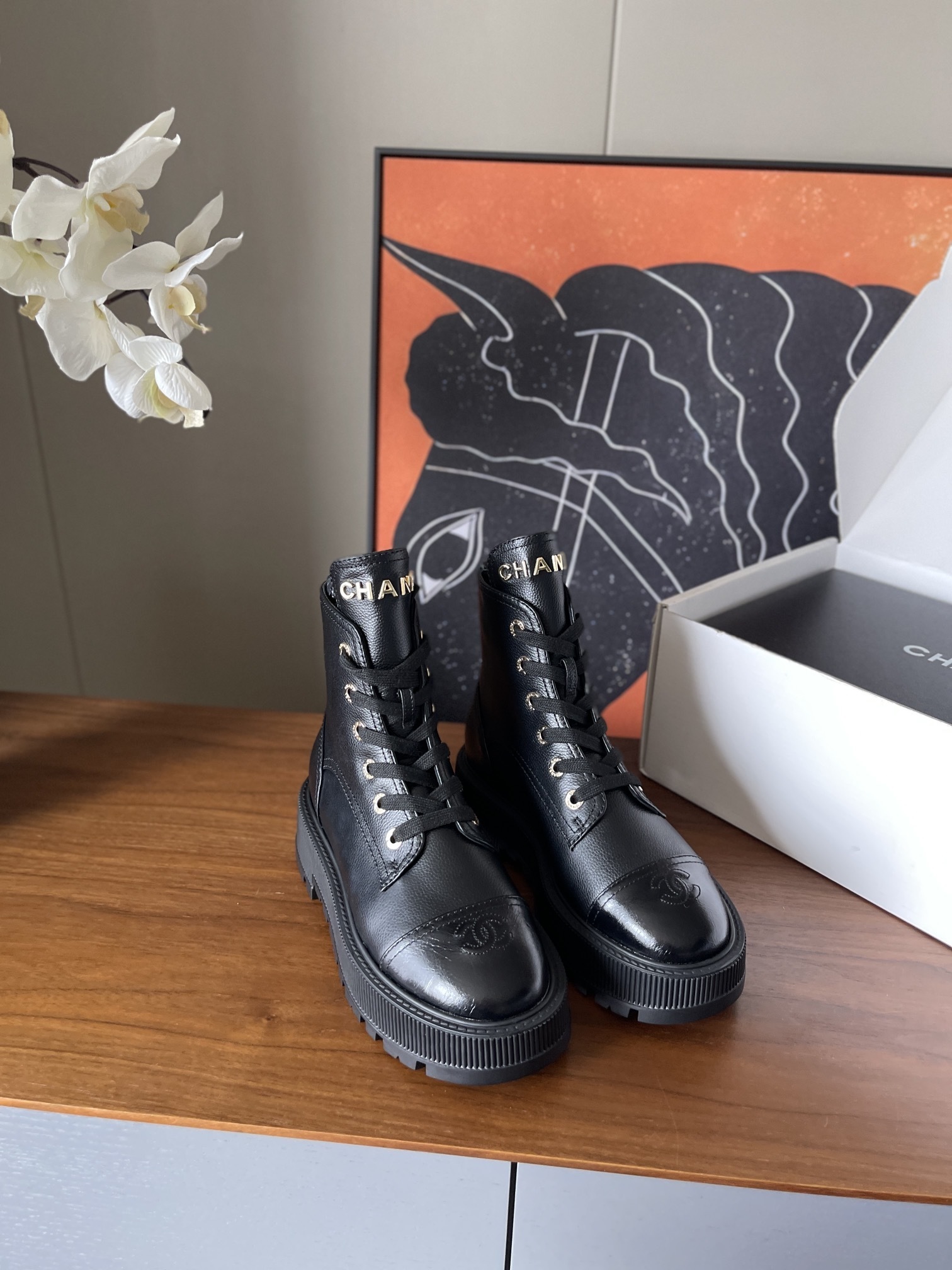 A pair of black Chanel grained leather combat boots with chunky platform soles and gold lettering on the tongue. - Hình 2