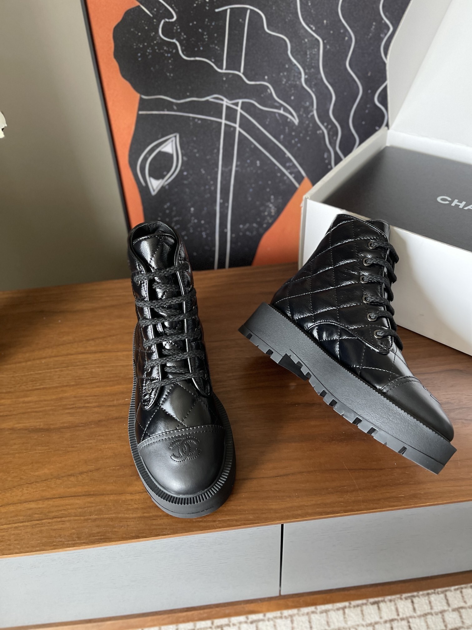 Pair of black quilted patent leather combat boots with chunky soles and logo toe caps on a wooden surface - Hình 8