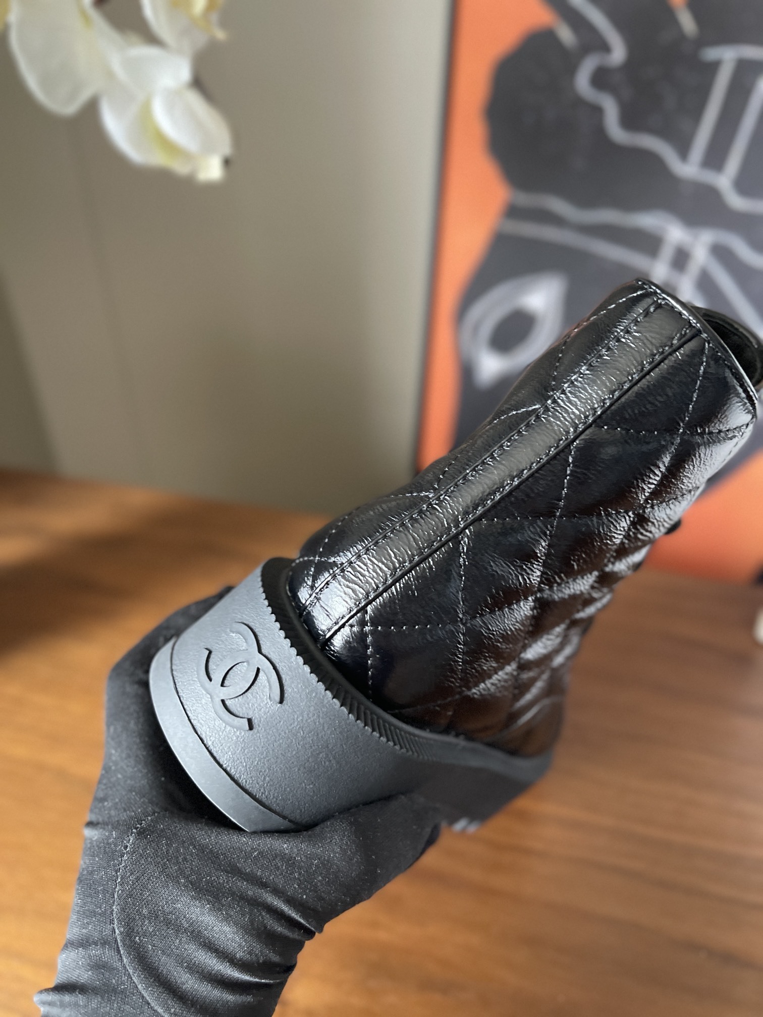 Pair of black quilted patent leather combat boots with chunky soles and logo toe caps on a wooden surface - Hình 7