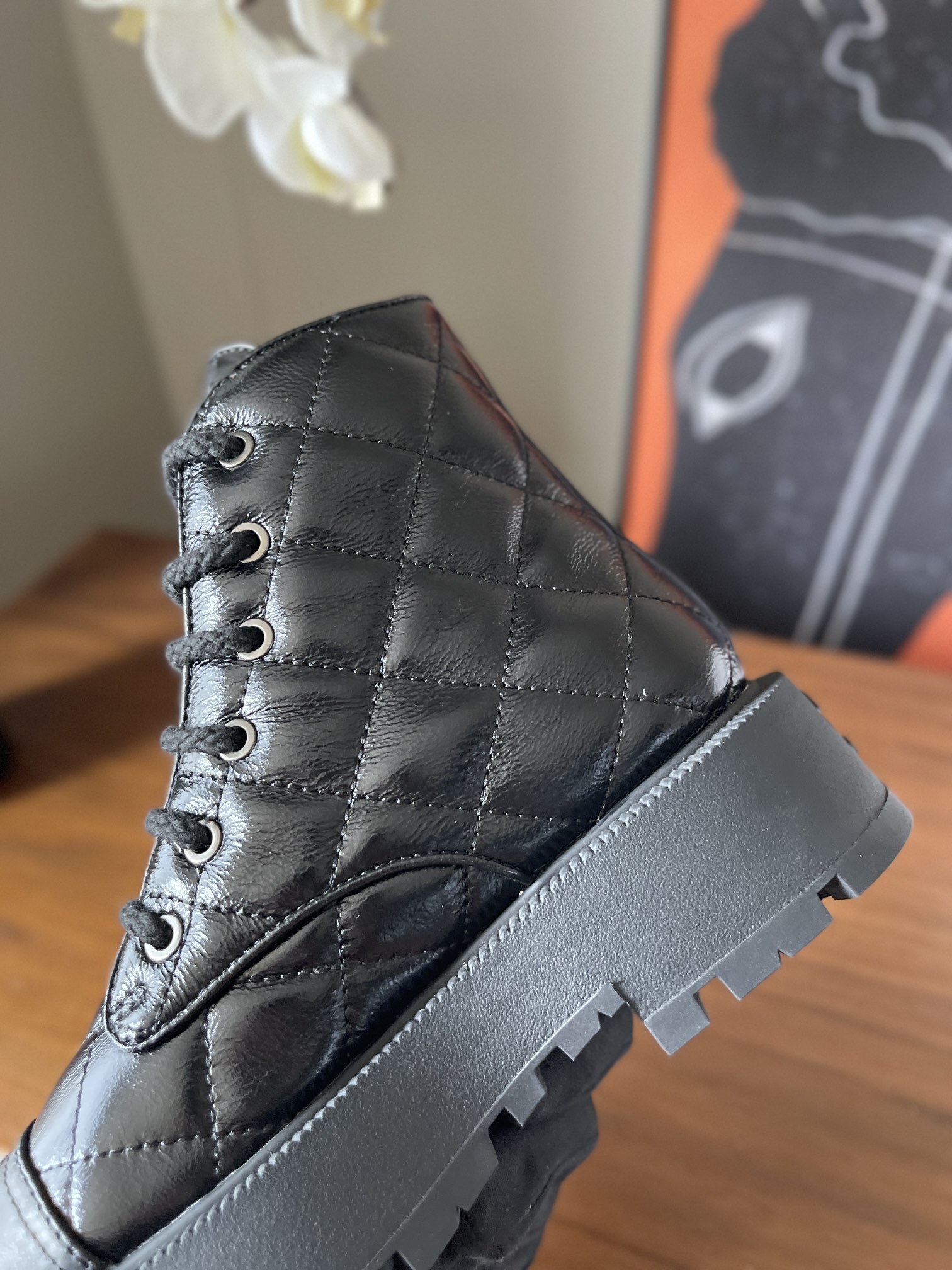 Pair of black quilted patent leather combat boots with chunky soles and logo toe caps on a wooden surface - Hình 6