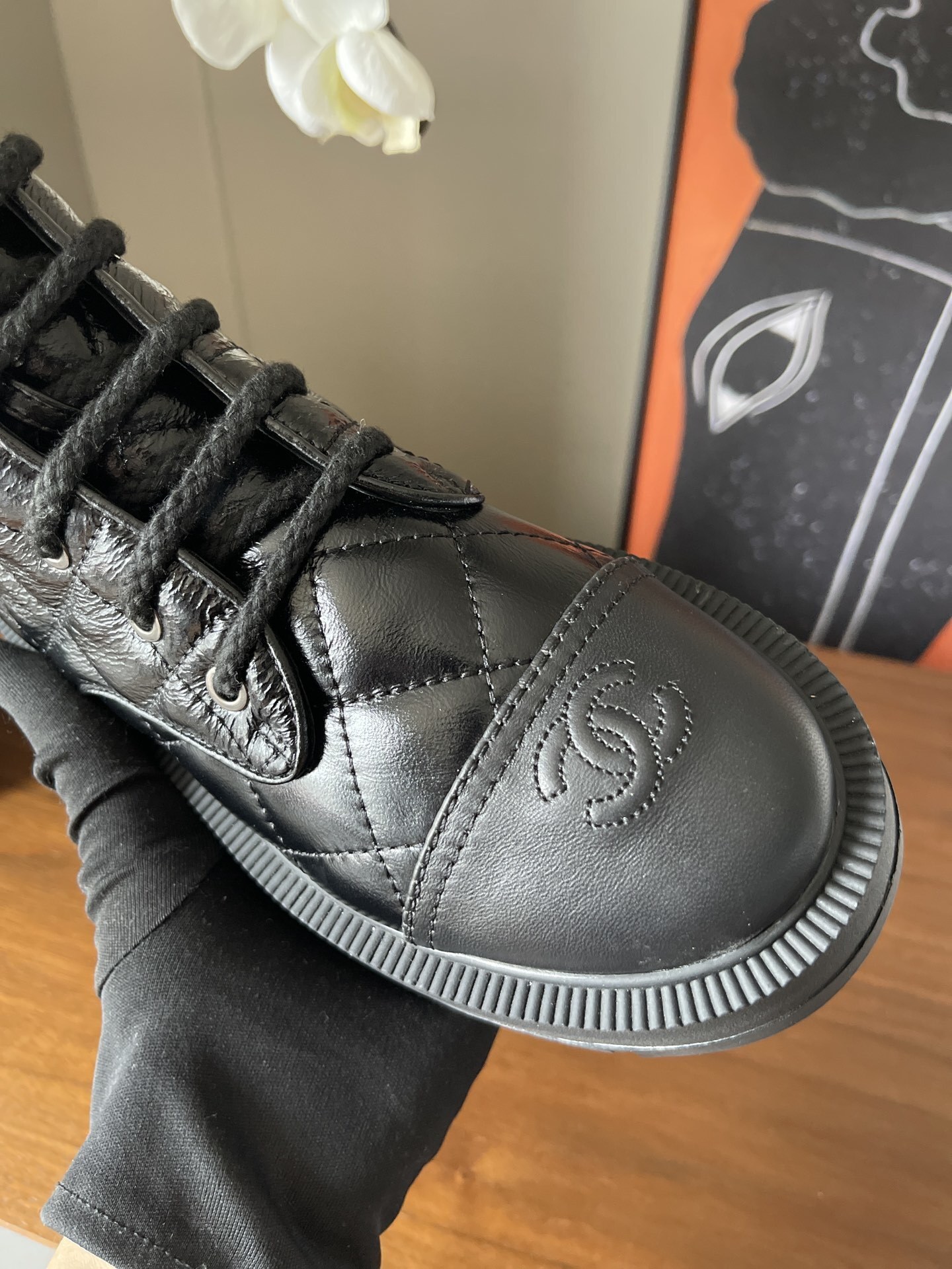 Pair of black quilted patent leather combat boots with chunky soles and logo toe caps on a wooden surface - Hình 5