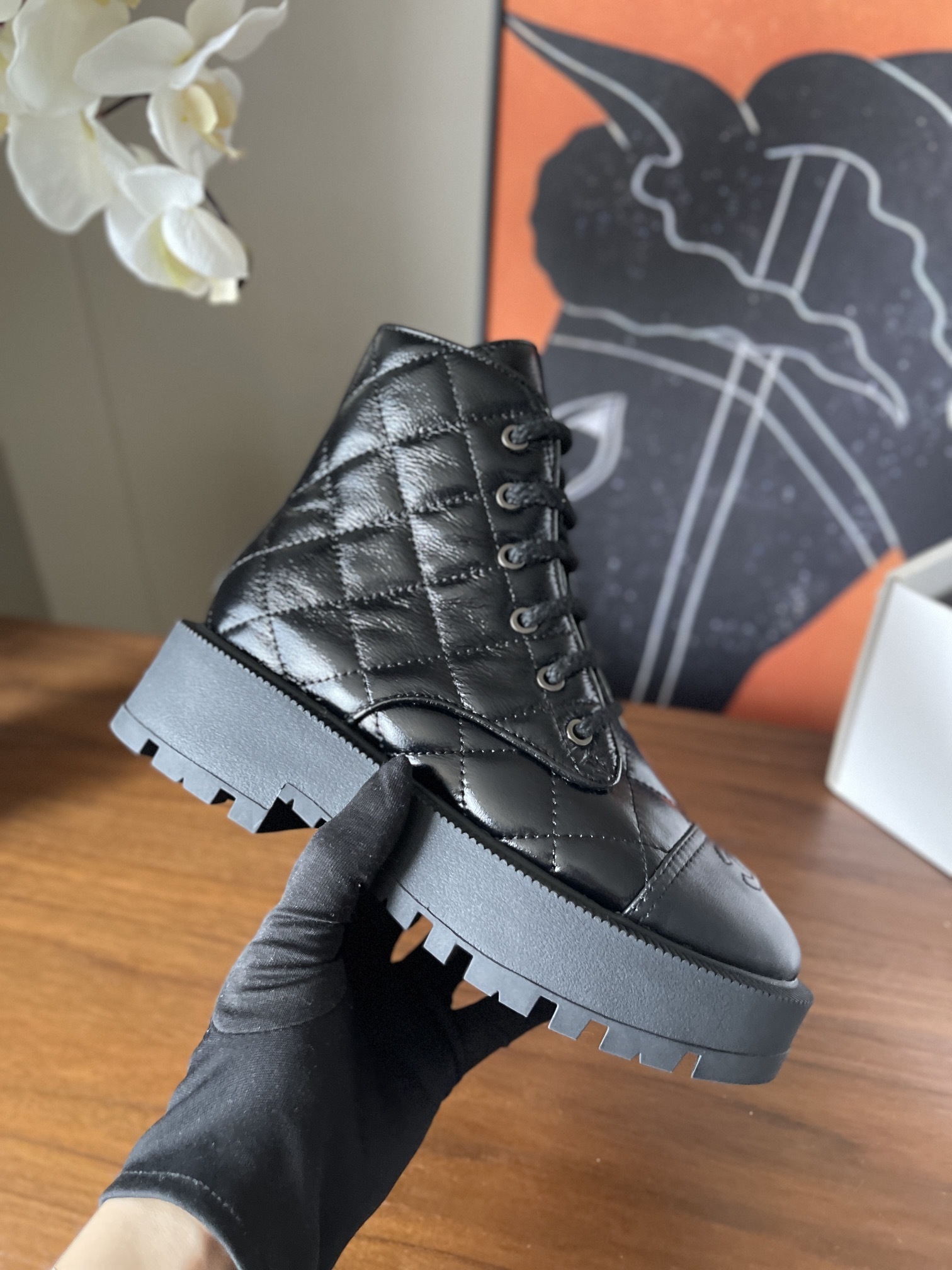 Pair of black quilted patent leather combat boots with chunky soles and logo toe caps on a wooden surface - Hình 4