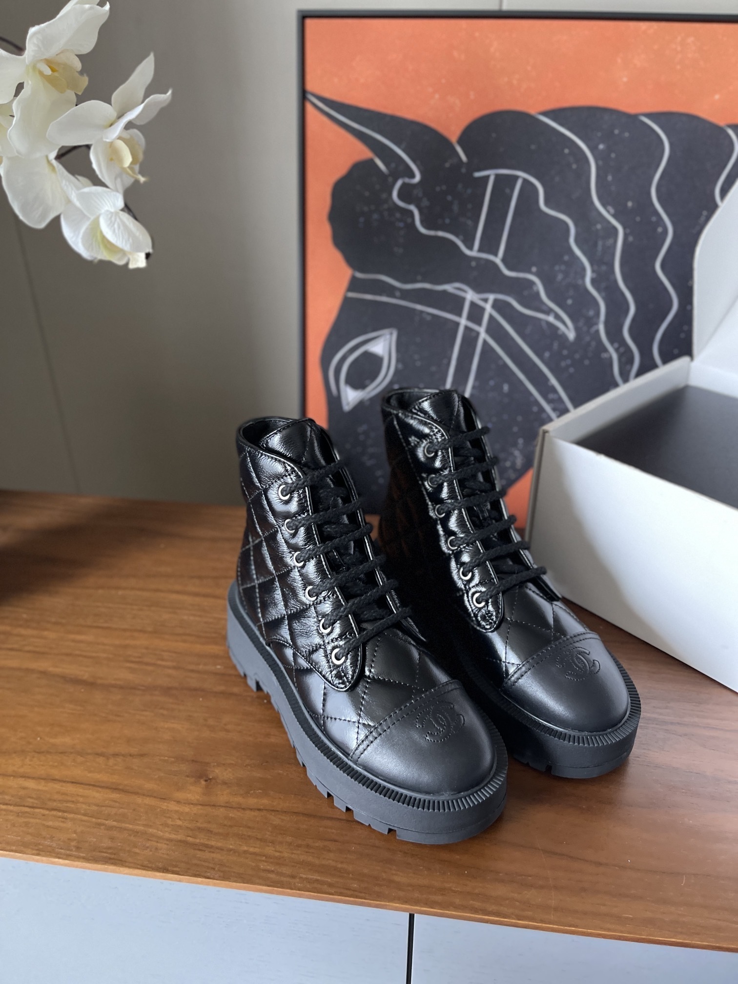 Pair of black quilted patent leather combat boots with chunky soles and logo toe caps on a wooden surface - Hình 2