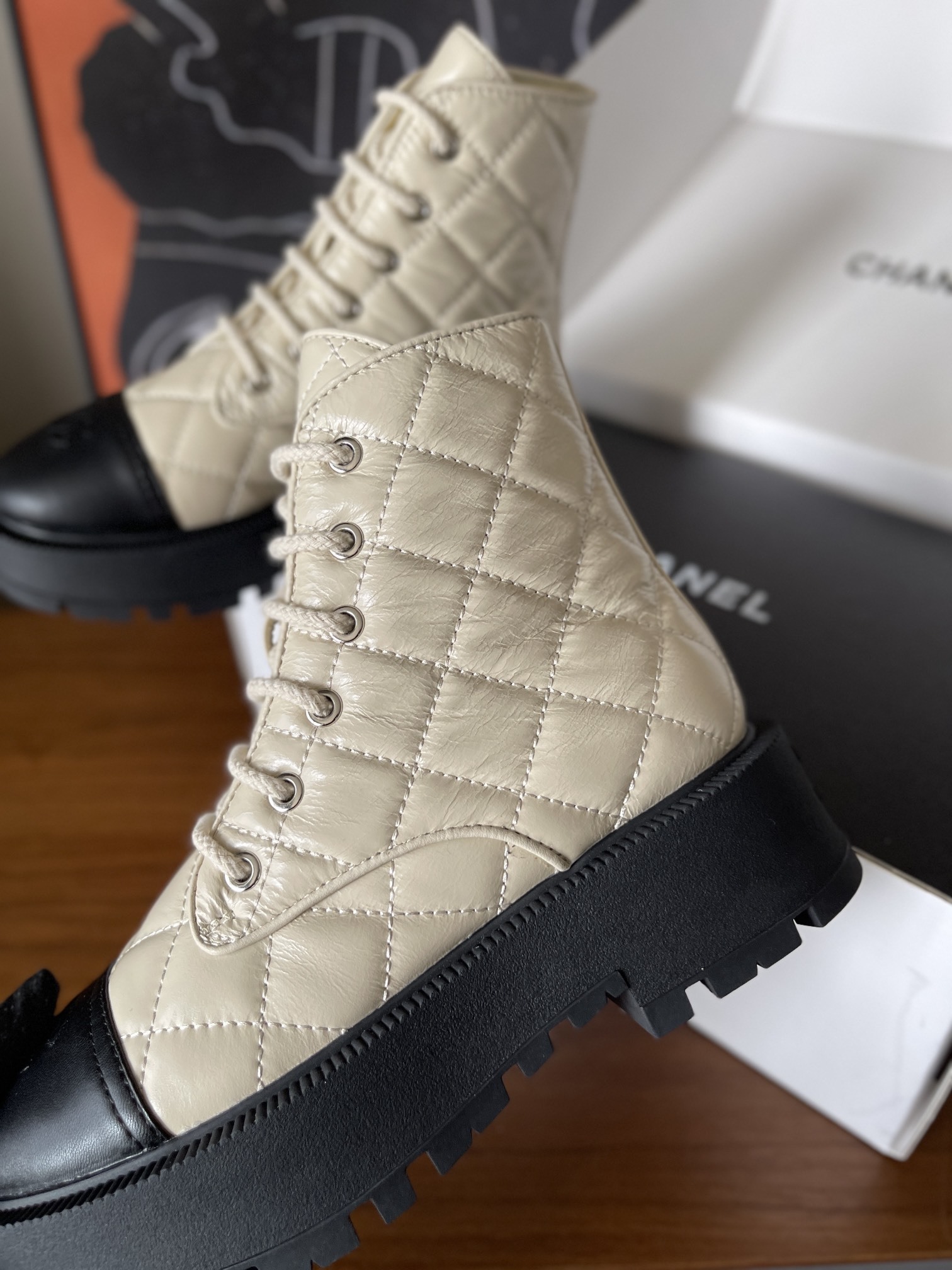 Pair of luxury quilted beige leather combat boots with black toe caps and chunky platform soles displayed on a wooden surface. - Hình 6