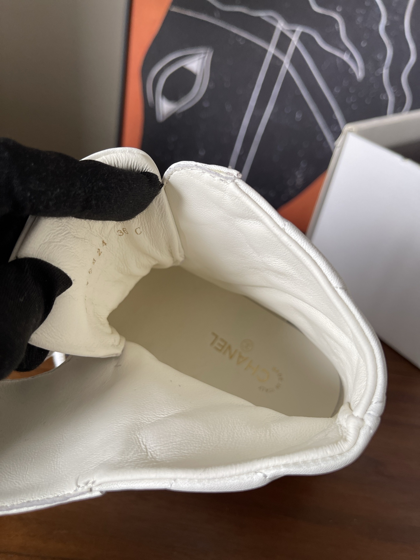 Pair of white quilted ankle boots with black cap toes and gold chain logo detail on a wooden surface - Hình 8