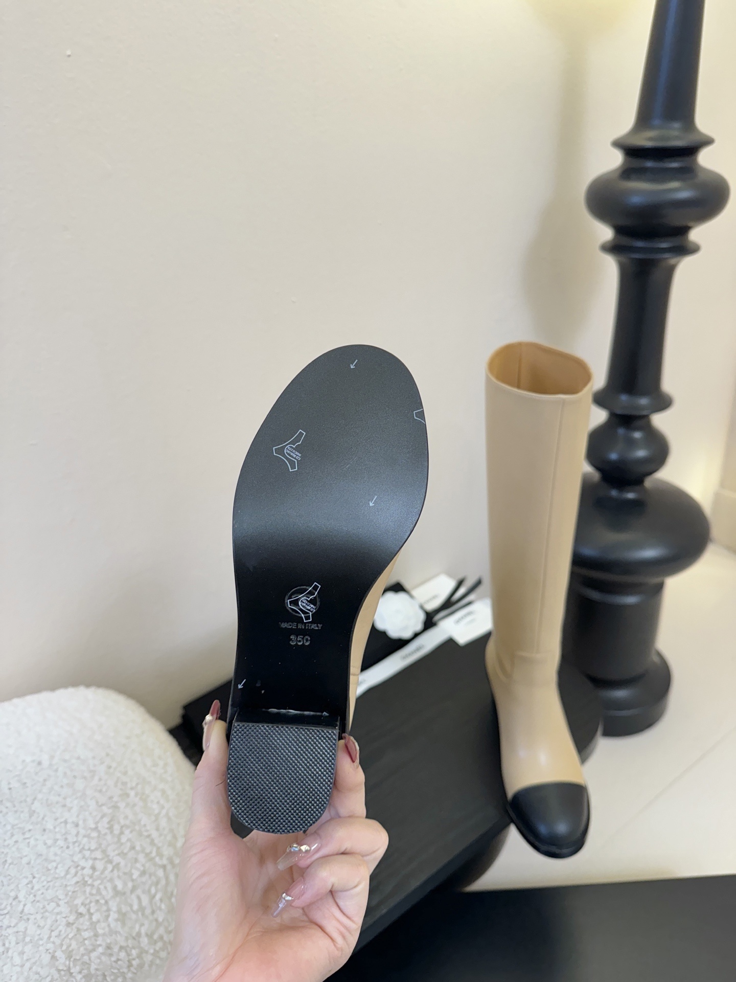 Chanel beige leather knee-high boots with black cap toes and white CC logo on a black display stand - Hình 9