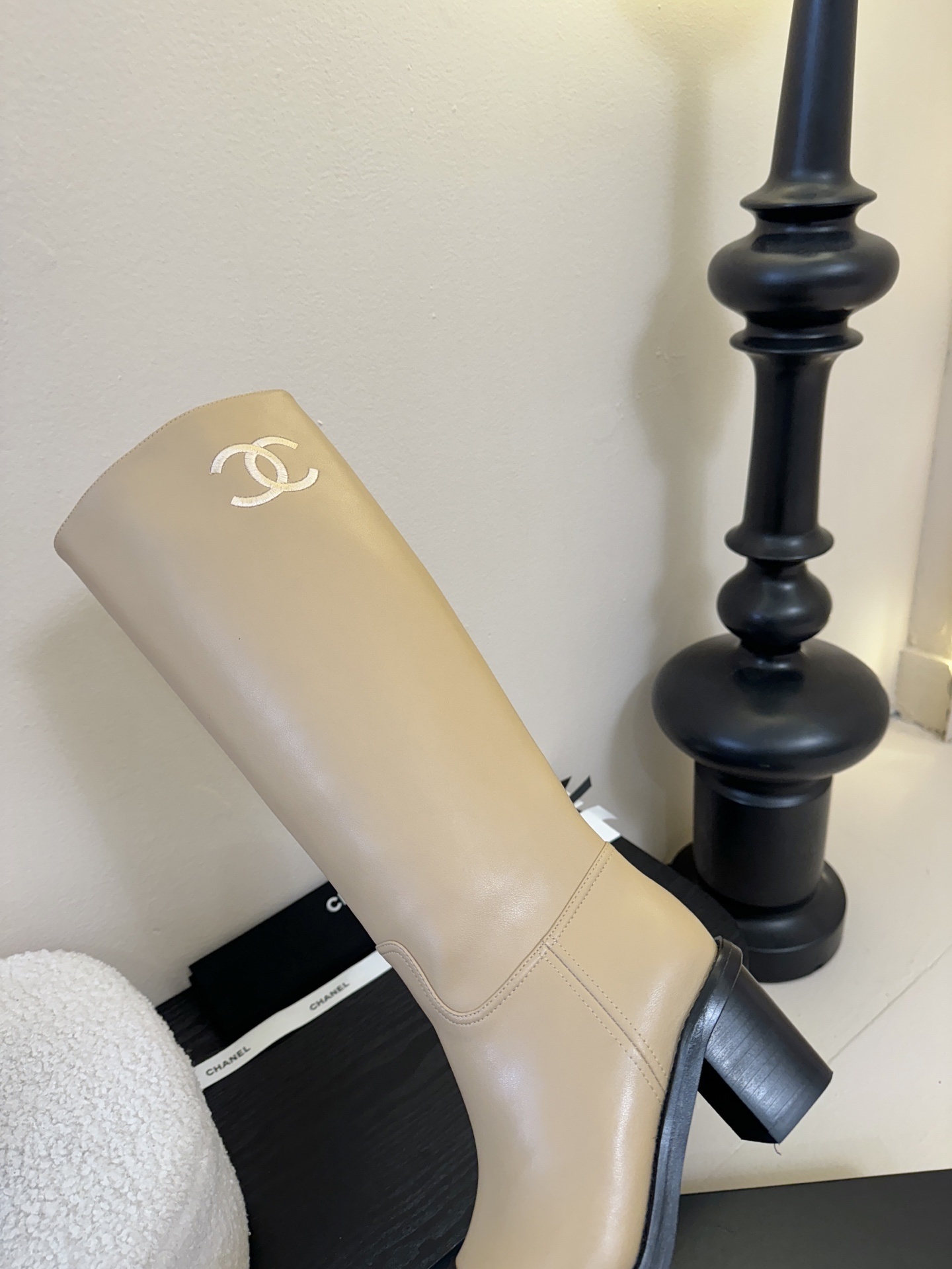 Chanel beige leather knee-high boots with black cap toes and white CC logo on a black display stand - Hình 8