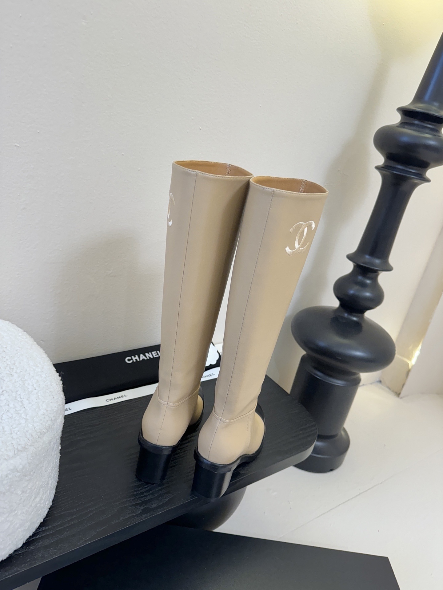 Chanel beige leather knee-high boots with black cap toes and white CC logo on a black display stand - Hình 7