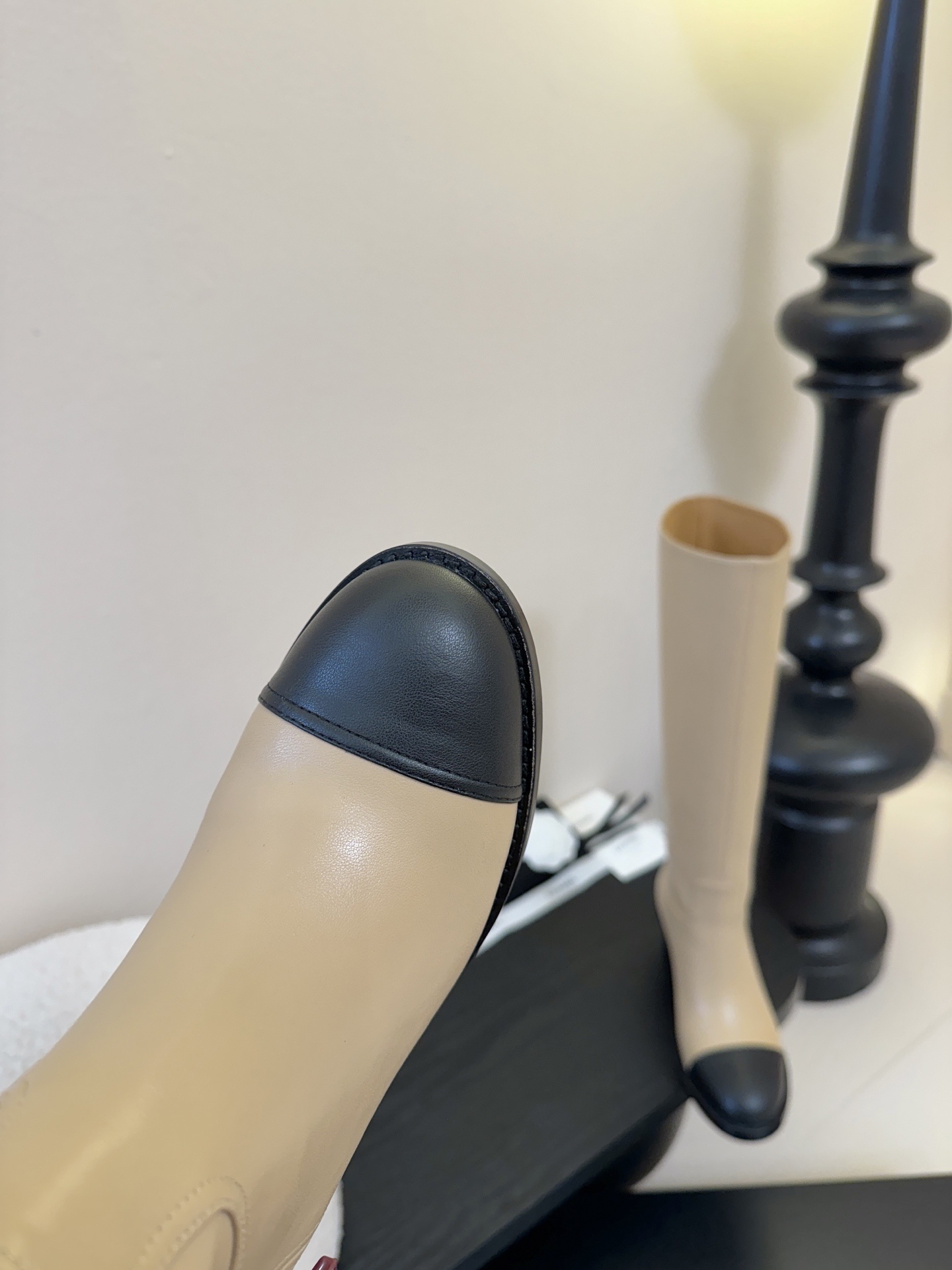 Chanel beige leather knee-high boots with black cap toes and white CC logo on a black display stand - Hình 6