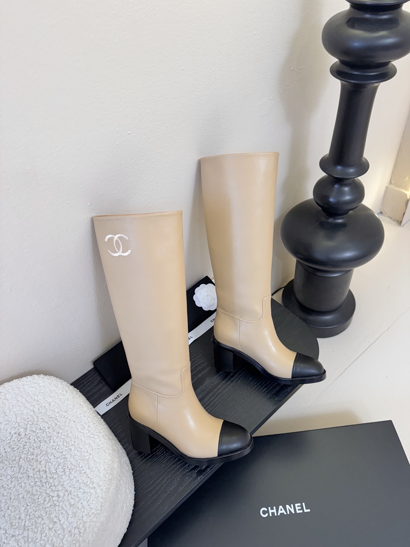 Chanel beige leather knee-high boots with black cap toes and white CC logo on a black display stand - Hình 4
