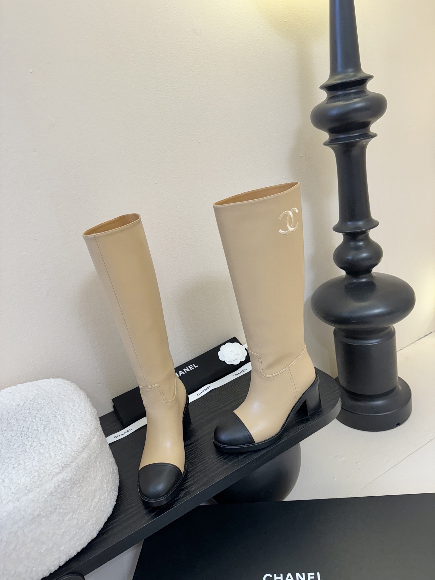 Chanel beige leather knee-high boots with black cap toes and white CC logo on a black display stand - Hình 3