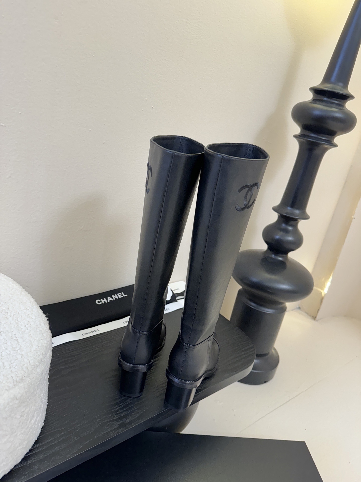 A pair of elegant Chanel black calfskin leather knee-high boots with an embroidered CC logo and block heels displayed on a black stand. - Hình 7