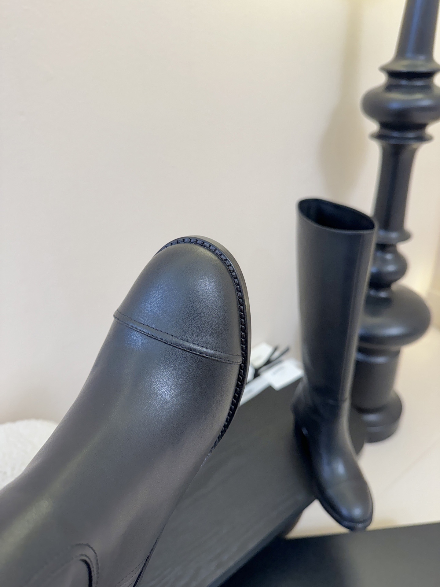 A pair of elegant Chanel black calfskin leather knee-high boots with an embroidered CC logo and block heels displayed on a black stand. - Hình 6