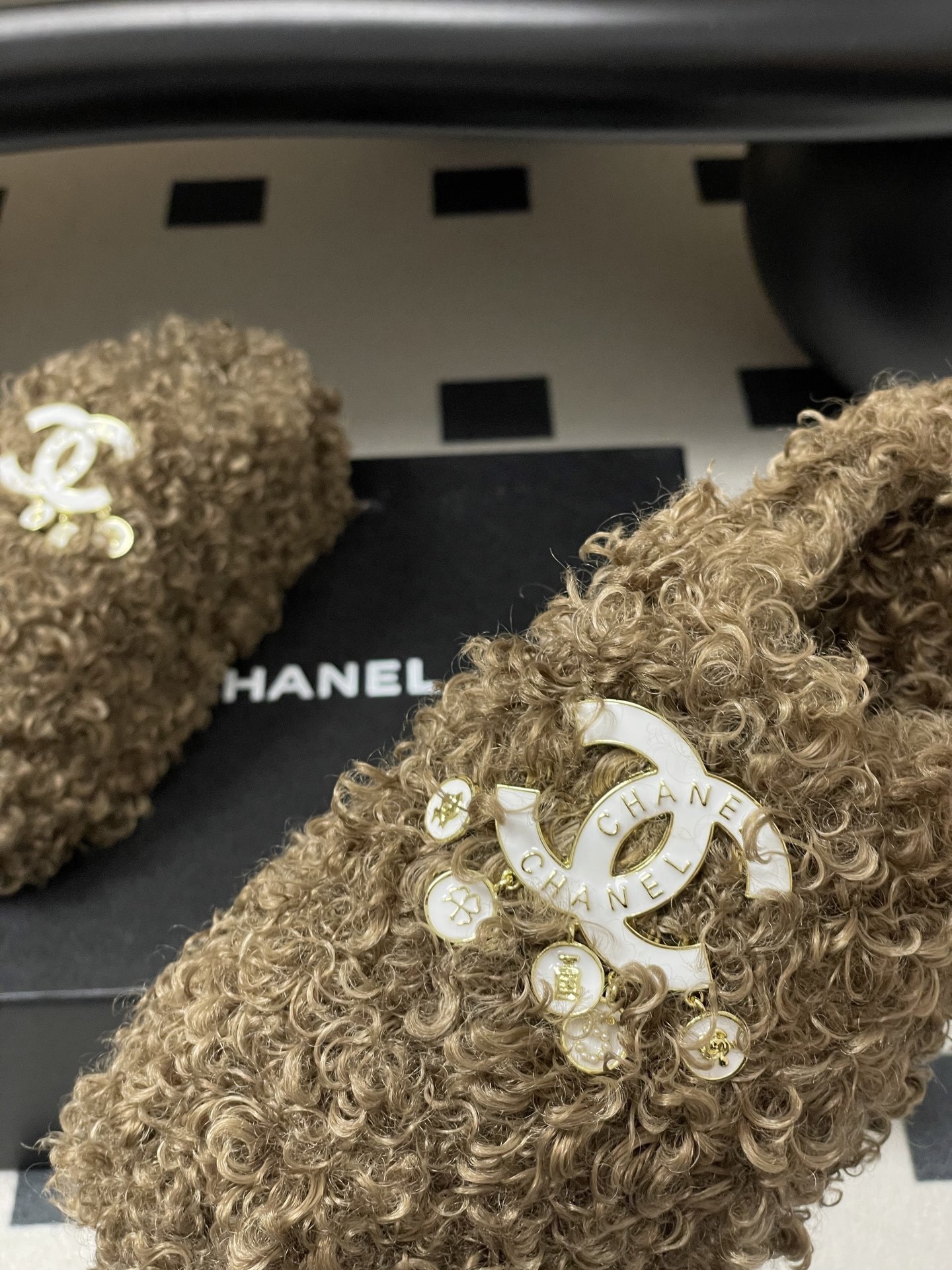A pair of luxury brown curly faux fur slippers featuring a white logo and gold dangling charms - Hình 9