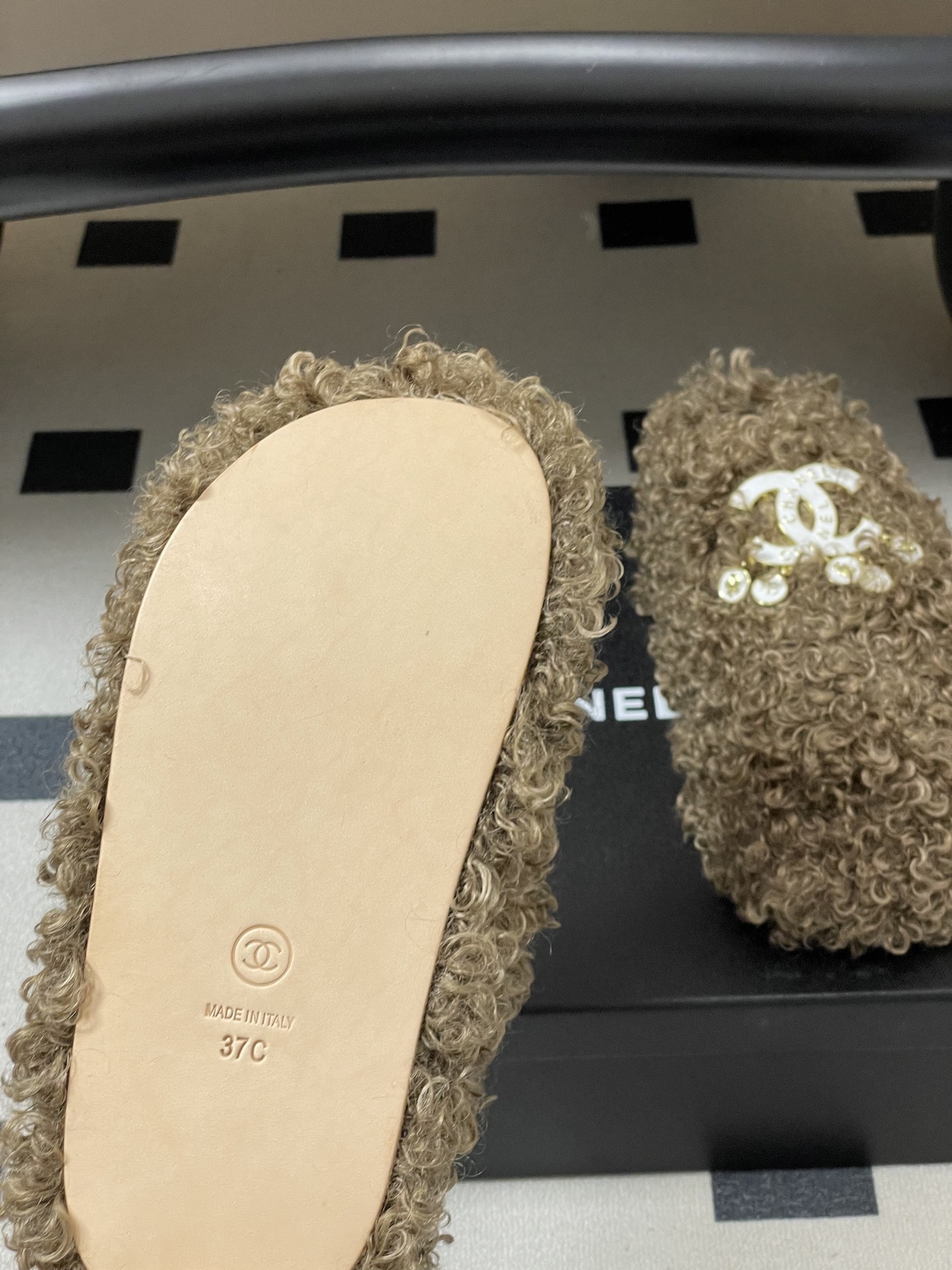 A pair of luxury brown curly faux fur slippers featuring a white logo and gold dangling charms - Hình 8