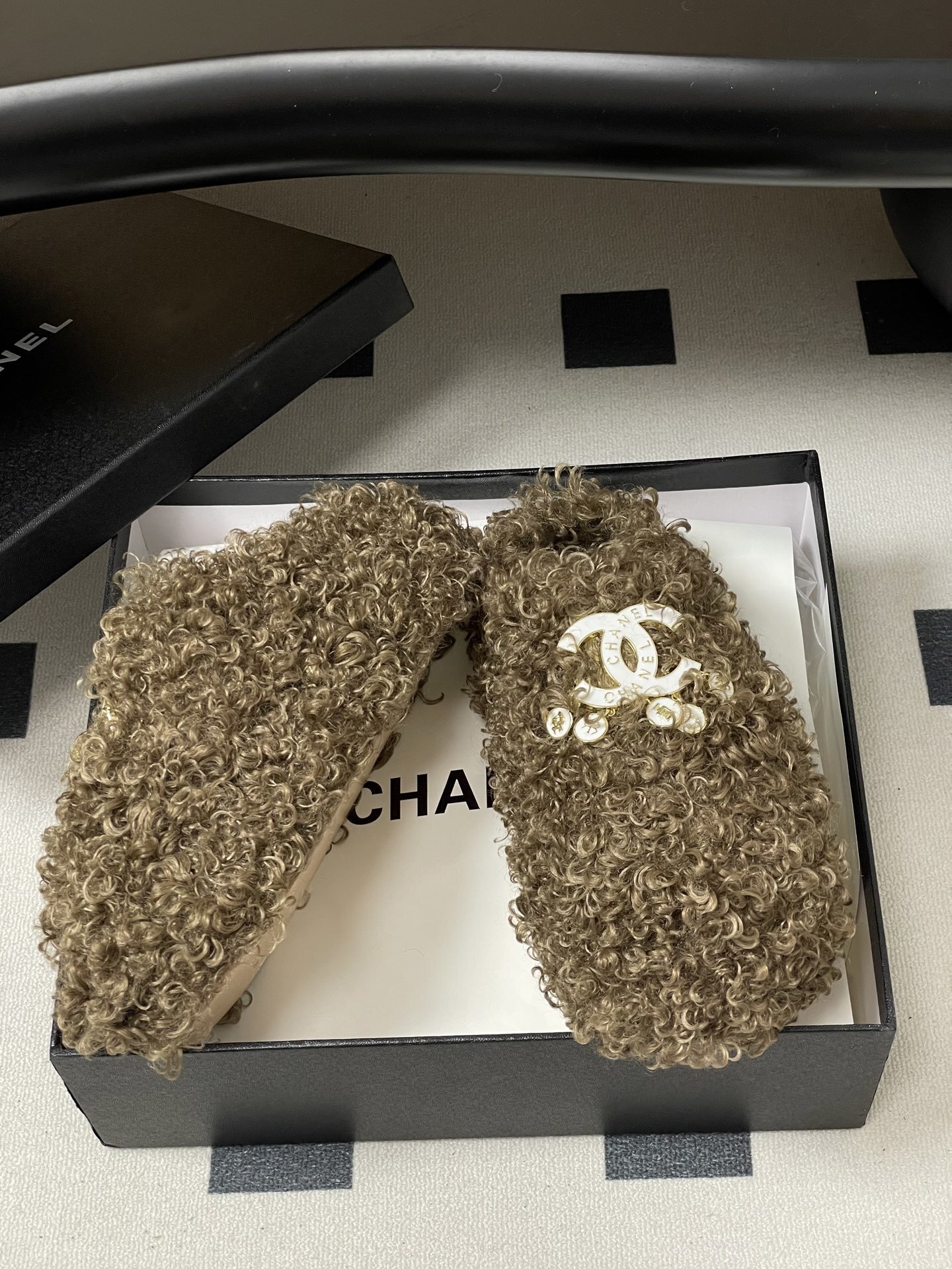A pair of luxury brown curly faux fur slippers featuring a white logo and gold dangling charms - Hình 6