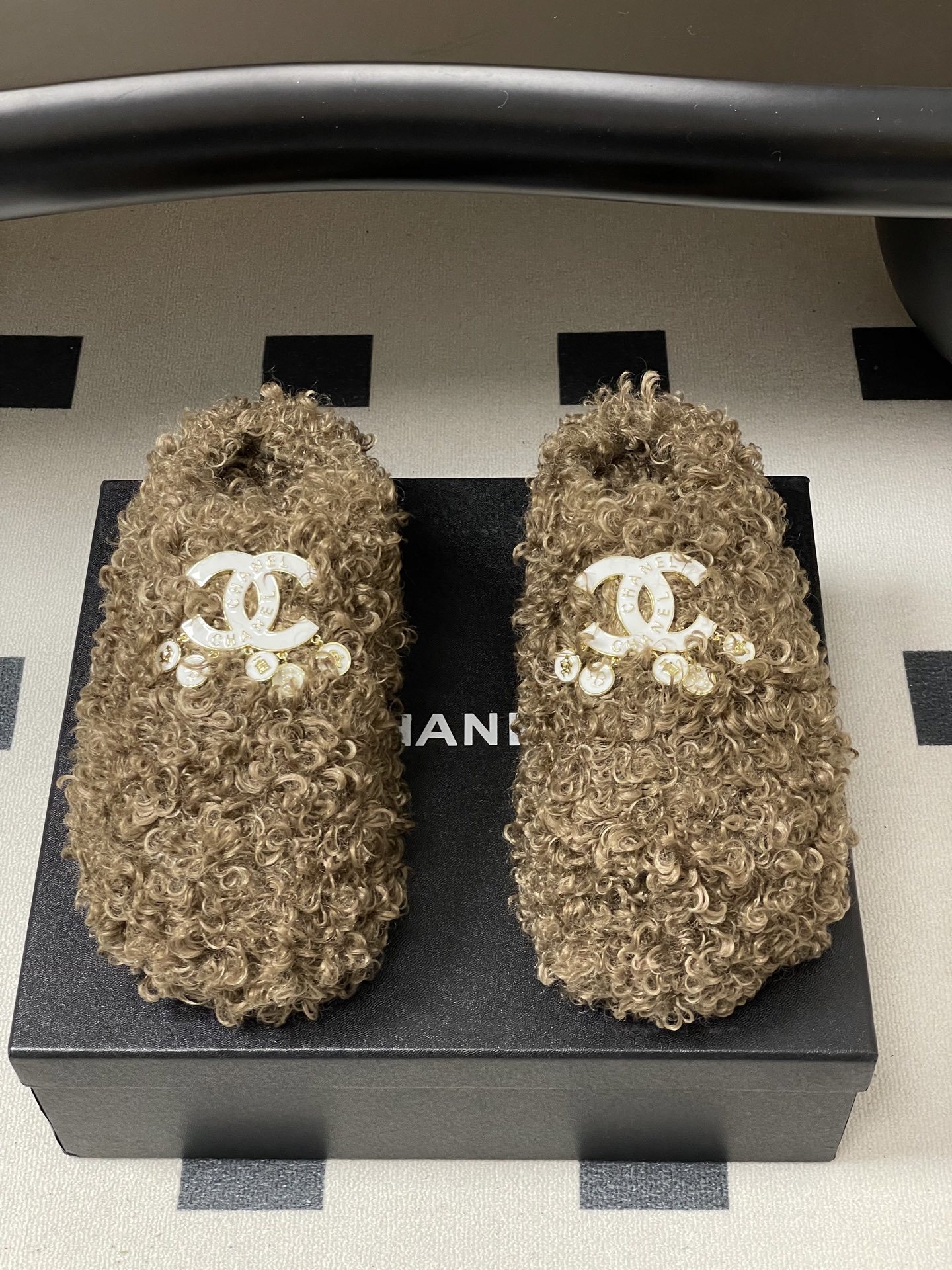 A pair of luxury brown curly faux fur slippers featuring a white logo and gold dangling charms - Hình 5
