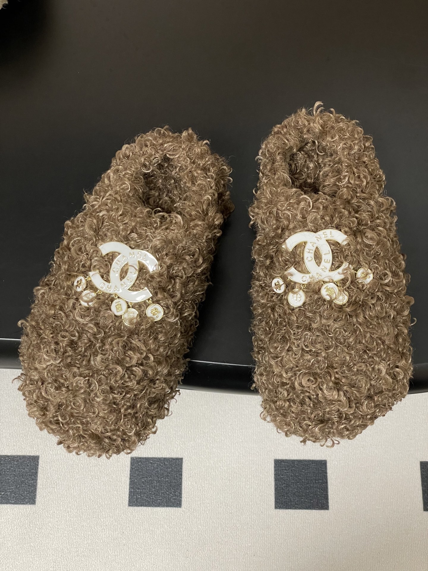 A pair of luxury brown curly faux fur slippers featuring a white logo and gold dangling charms - Hình 2