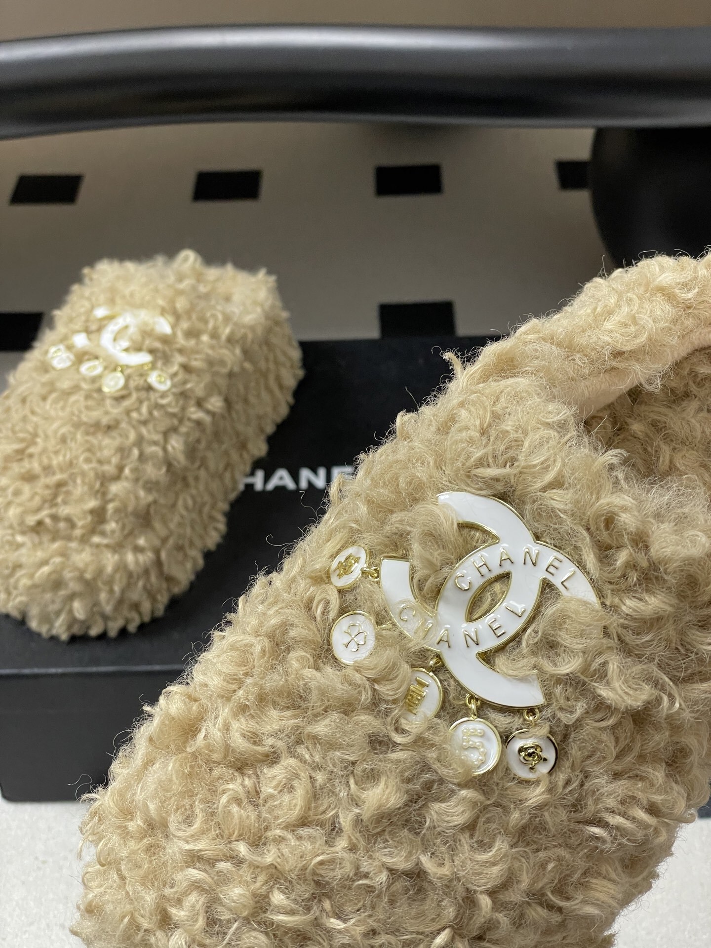 Pair of beige curly faux fur platform slippers featuring a white designer logo with hanging pearl charms on a black surface. - Hình 9