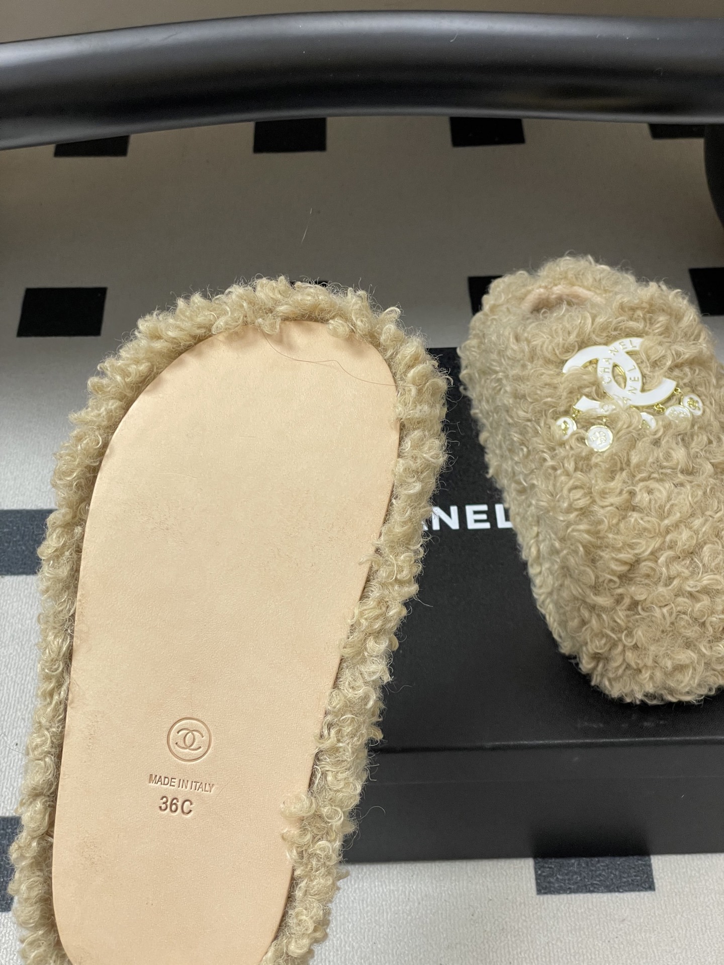 Pair of beige curly faux fur platform slippers featuring a white designer logo with hanging pearl charms on a black surface. - Hình 8