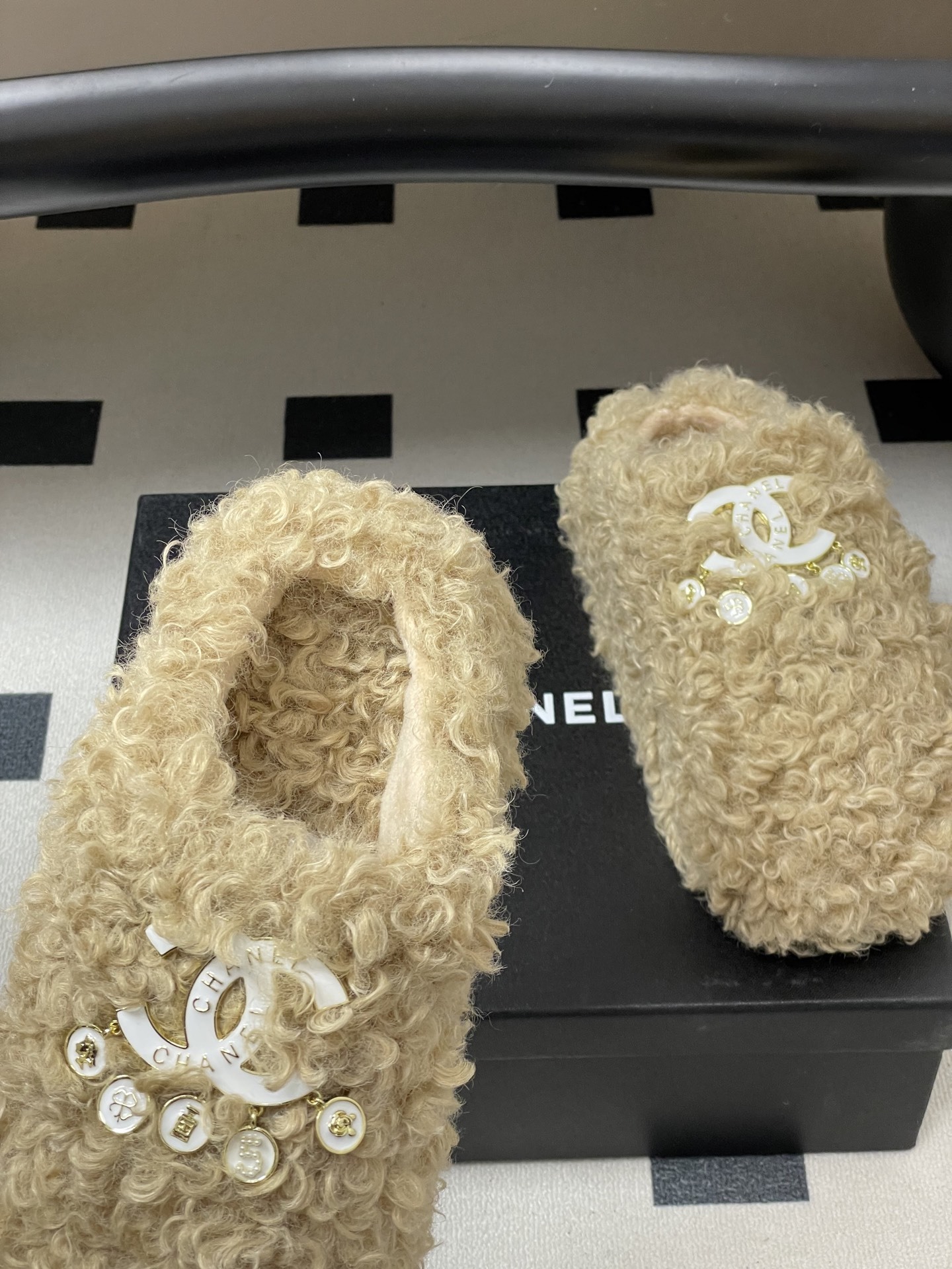 Pair of beige curly faux fur platform slippers featuring a white designer logo with hanging pearl charms on a black surface. - Hình 7